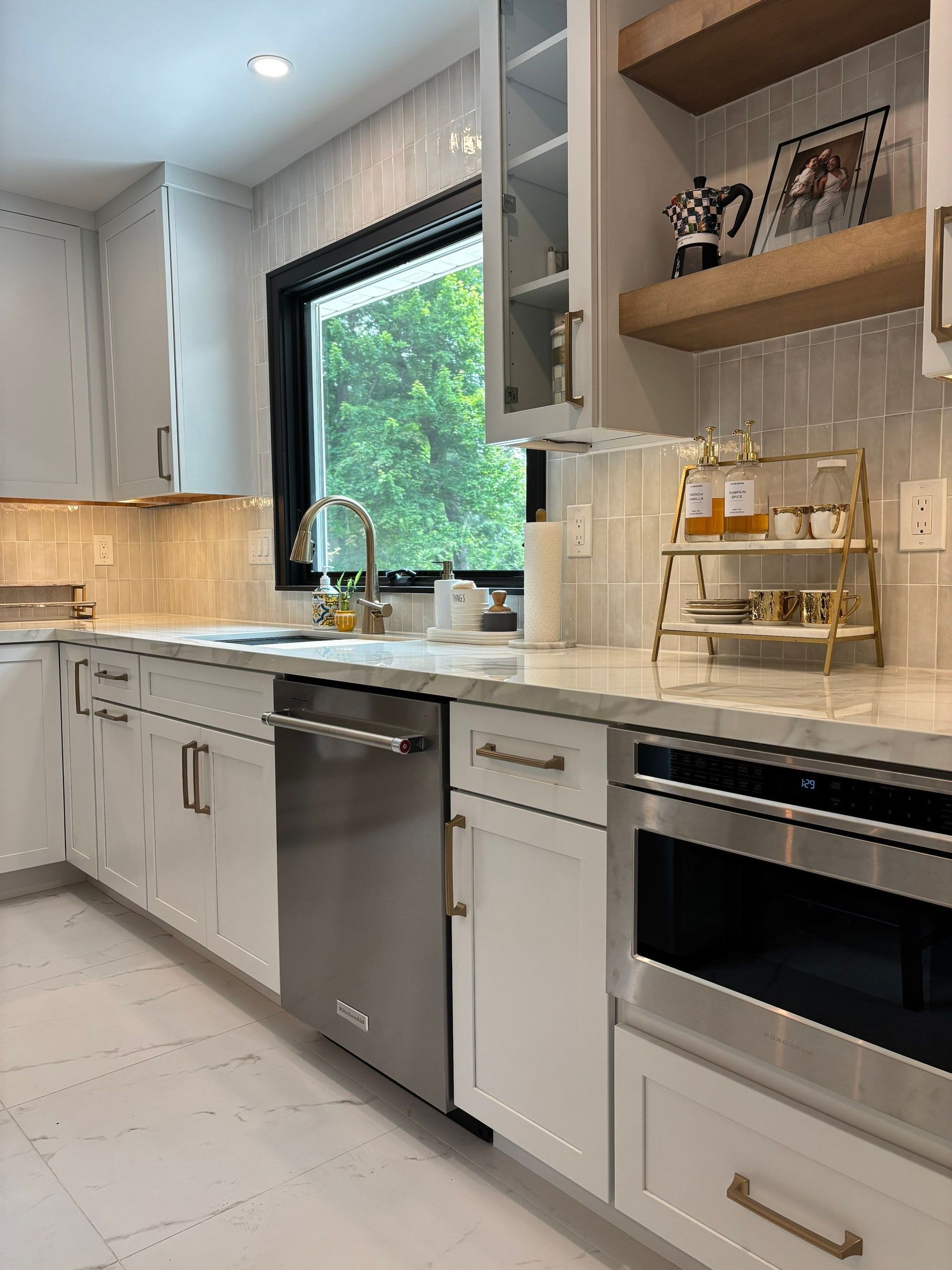 White kitchen with stainless steel appliances, light countertops, and a window with a green view.
