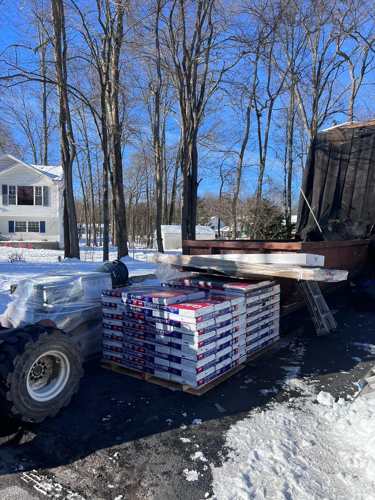 A forklift carries a pallet of red and white boxes on a snowy, sunny day.