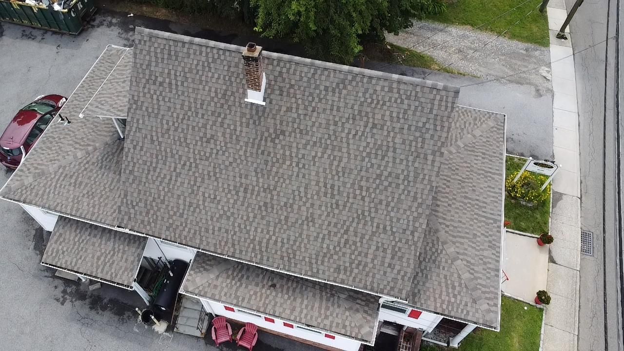 Overhead view of a building with a brown roof, chimney, and red car parked in front.