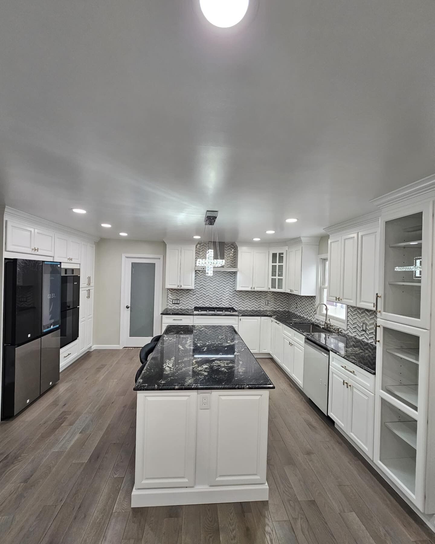 White kitchen with island, granite countertops, stainless steel appliances, and wood floors.