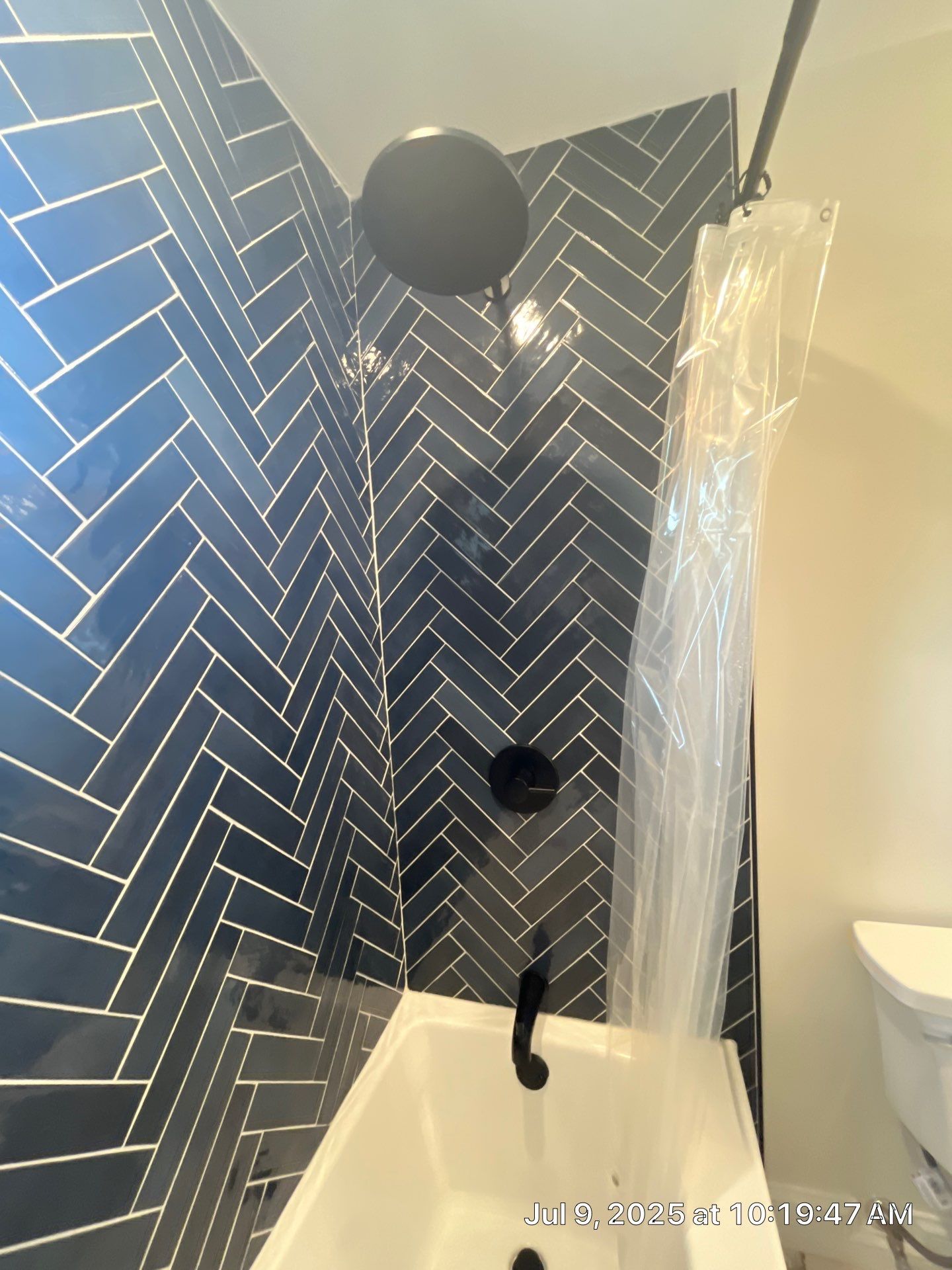 Dark blue herringbone tile shower with black fixtures and clear shower curtain.