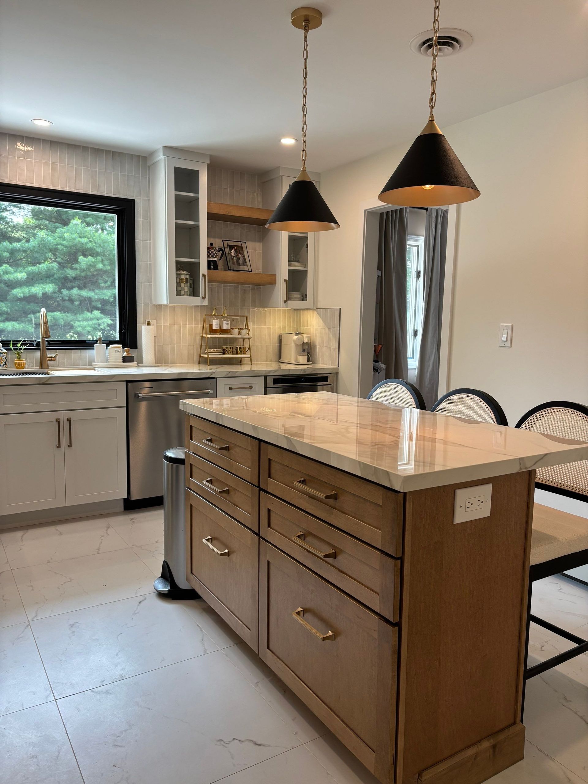 Kitchen with island and hanging lights; light-colored cabinets and countertops; stainless steel appliances; window with trees outside.