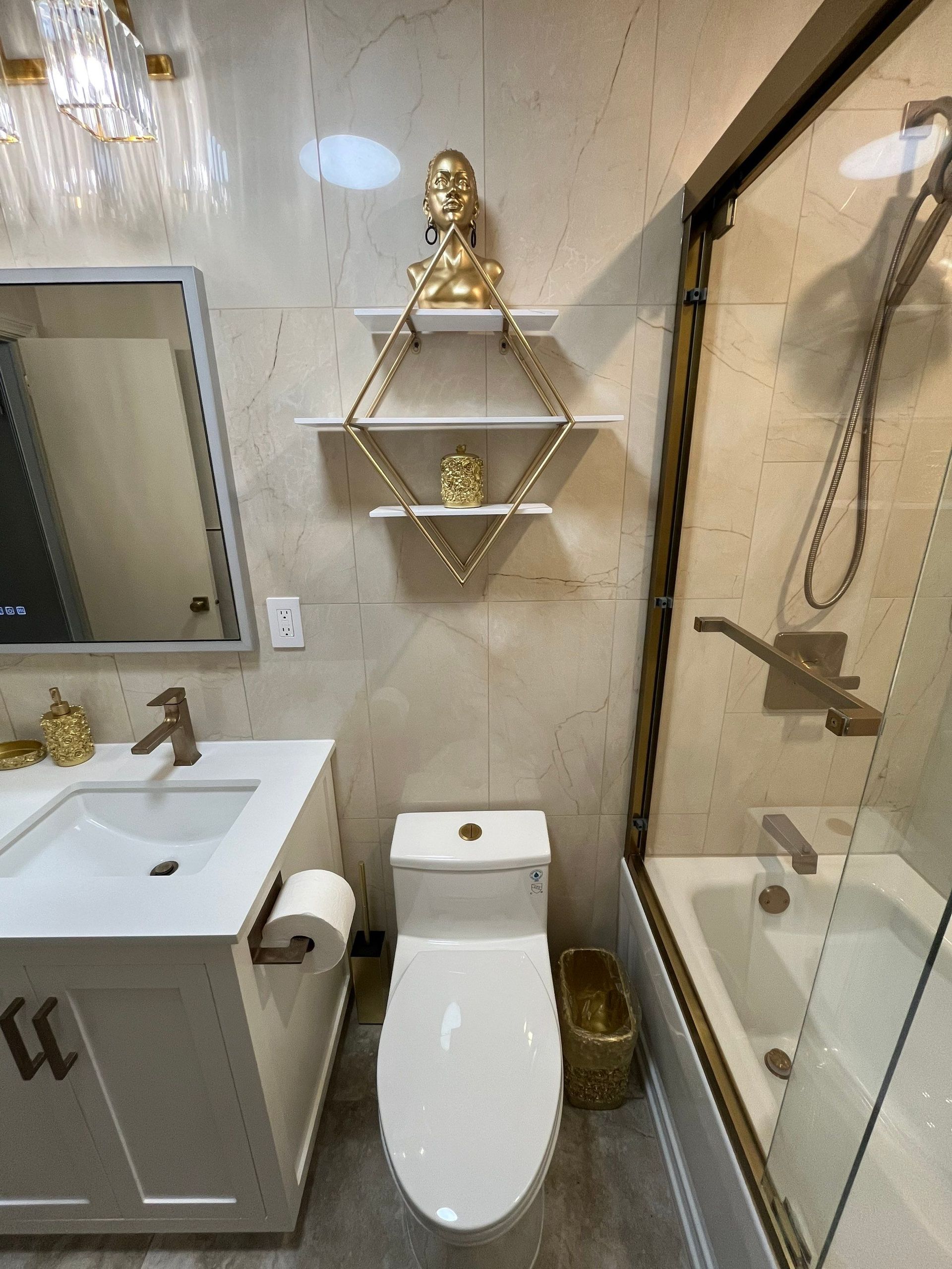 Bathroom with white toilet, vanity, and shower. Gold accents, Buddha statue on diamond shelf.