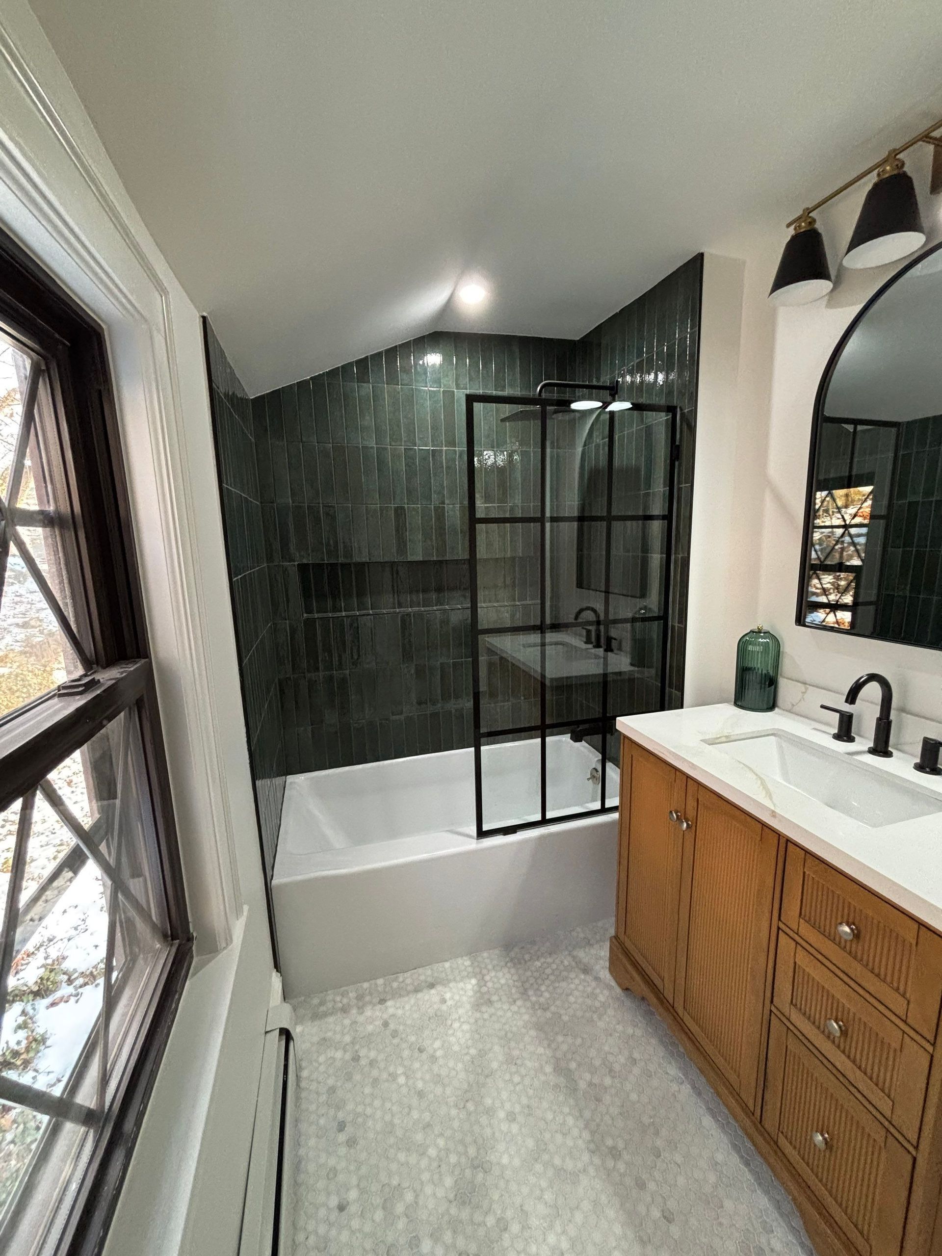 Bathroom with green tiled shower, wood vanity, black accents, and a window.