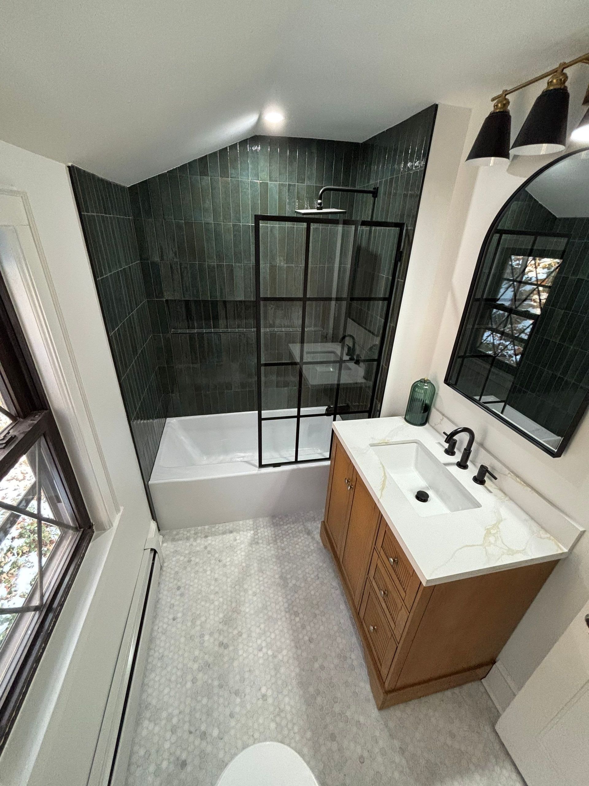 Small, modern bathroom with green tiled shower, wood vanity, and black accents.