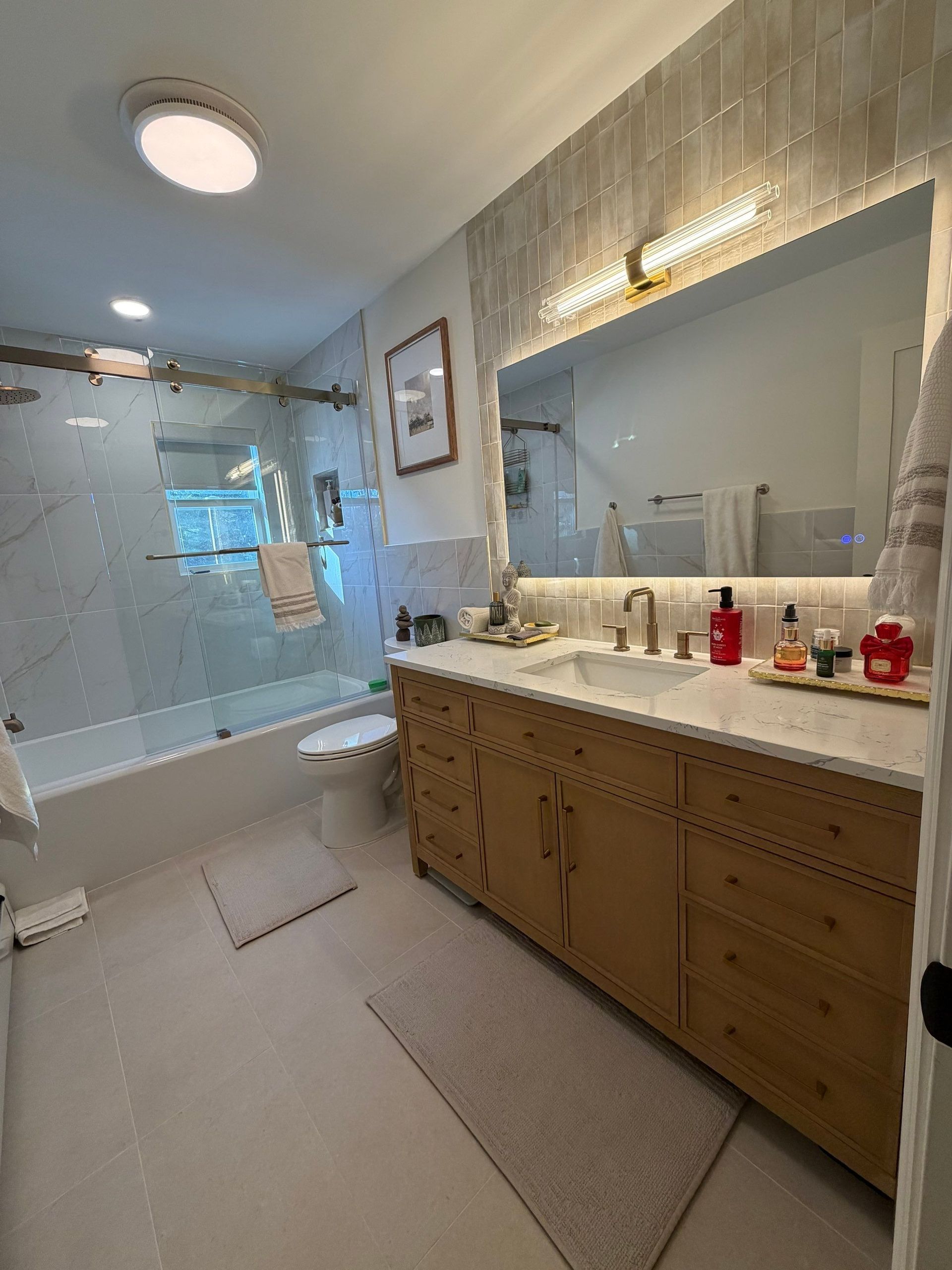 Bathroom with wooden vanity, large mirror, and glass shower. White and beige tiles, neutral color scheme.