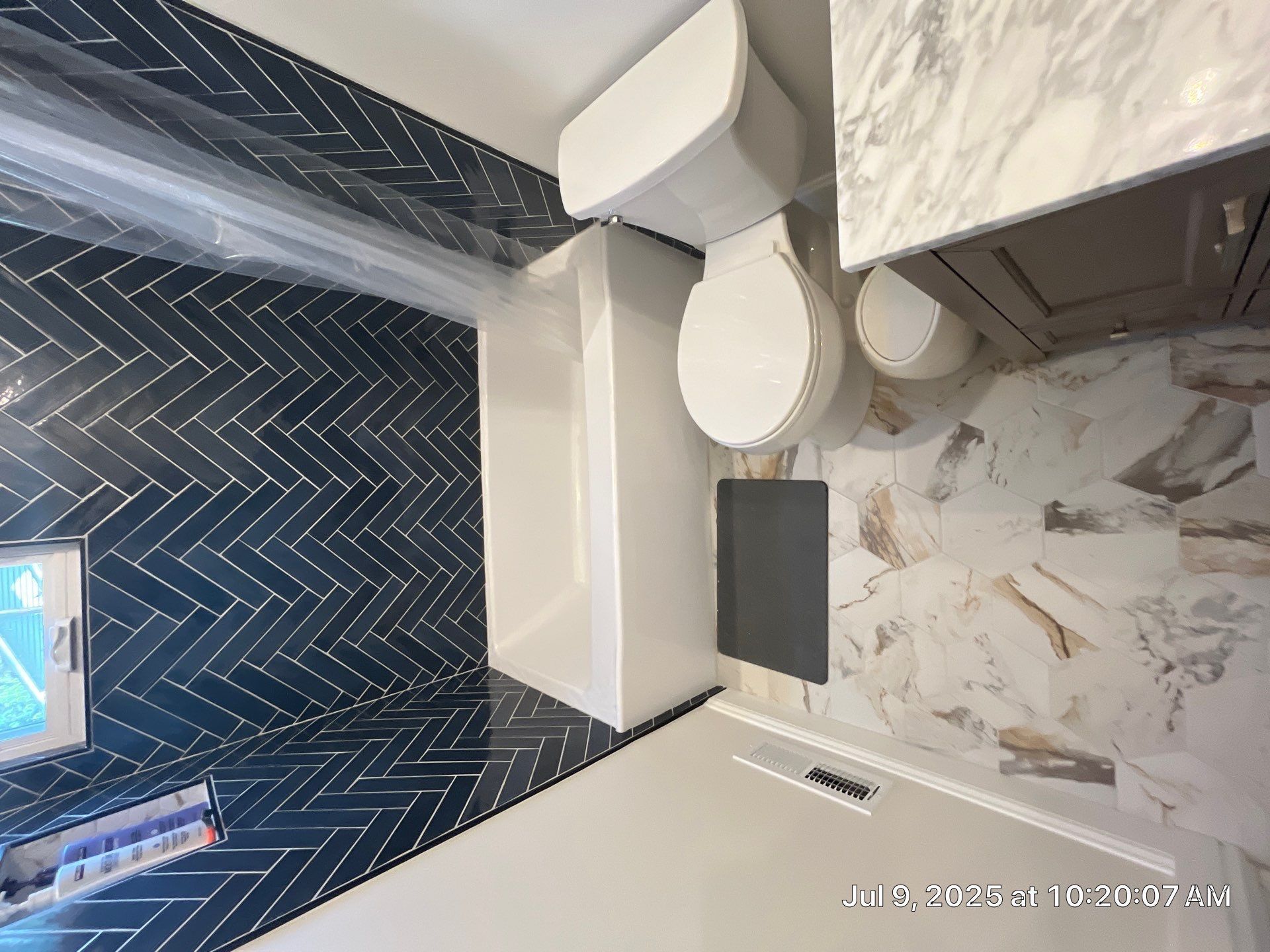 Bathroom with blue herringbone tile, white toilet and vanity, and light-colored wall tile.