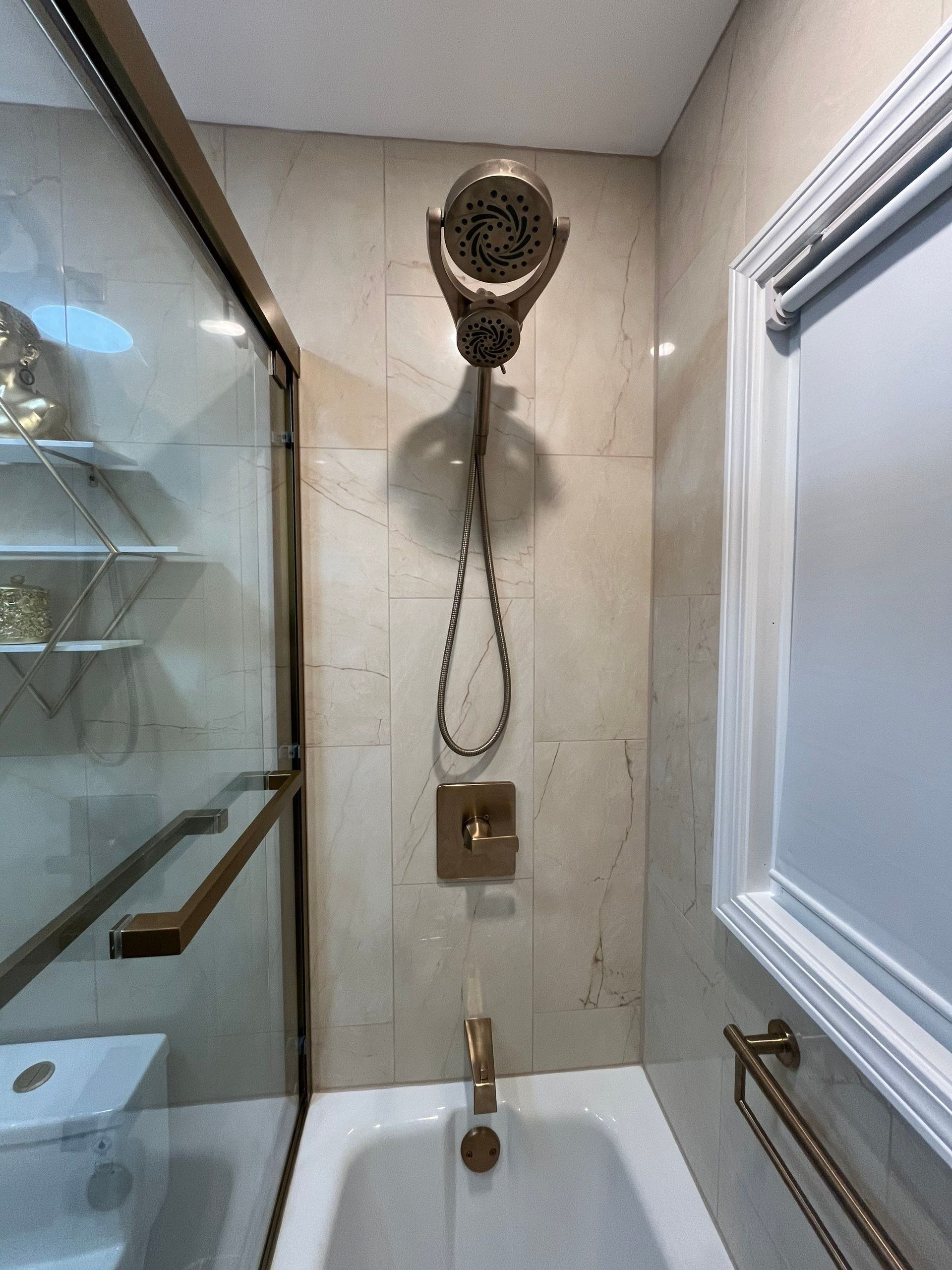 Gold shower fixtures in a tiled bathroom, including a rain shower head, hand shower, and tub spout.