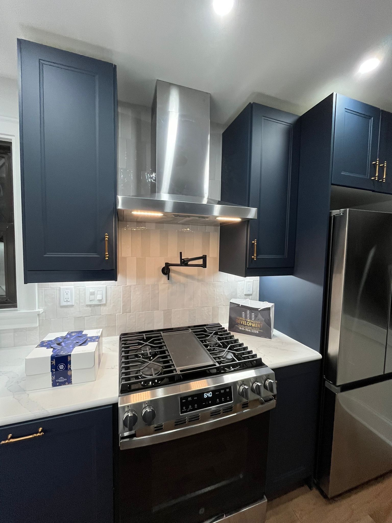 Modern navy blue kitchen with stainless steel appliances, white backsplash, and a gas range.