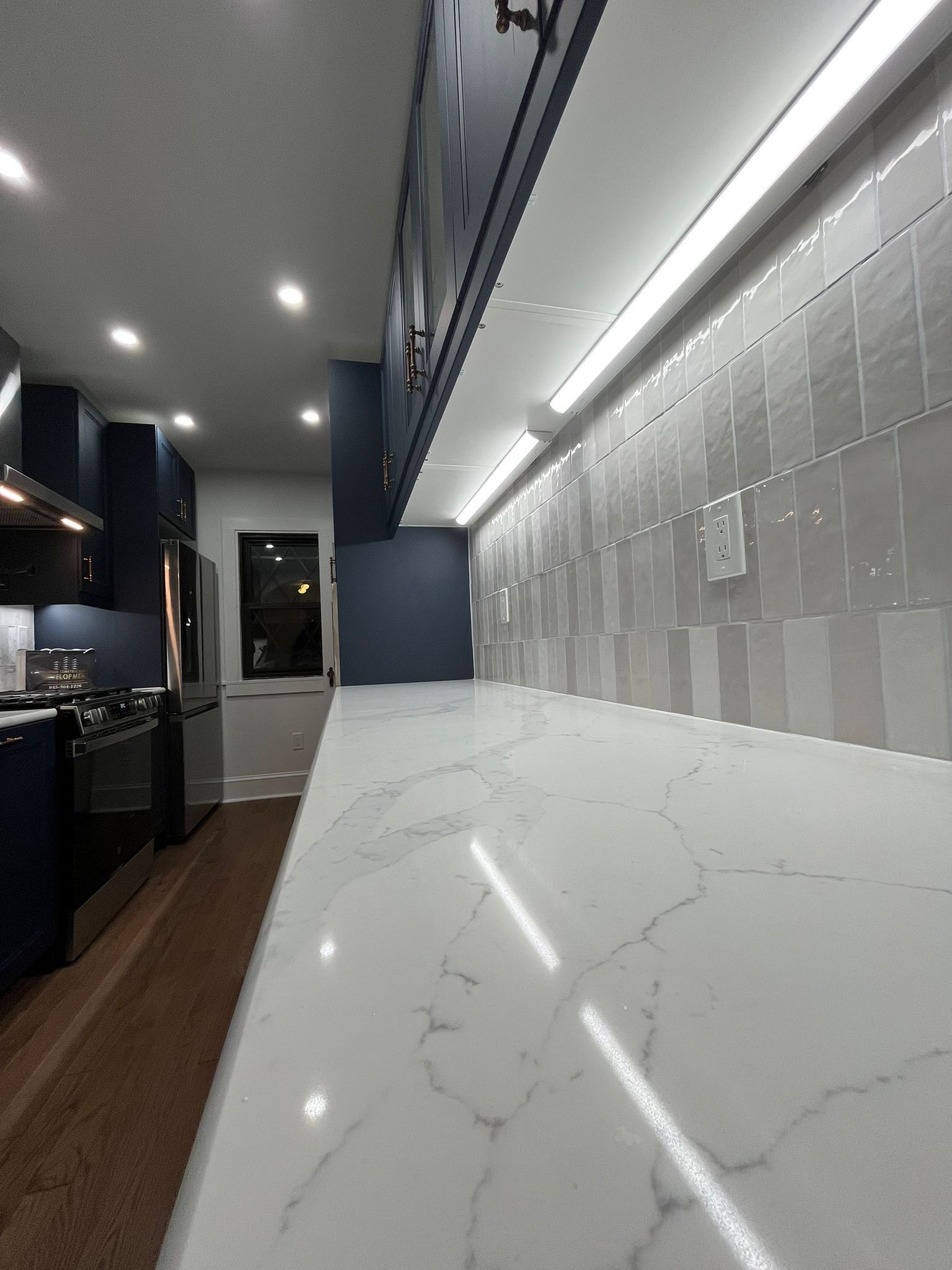 Modern kitchen with white countertop, gray backsplash, and navy blue cabinets.