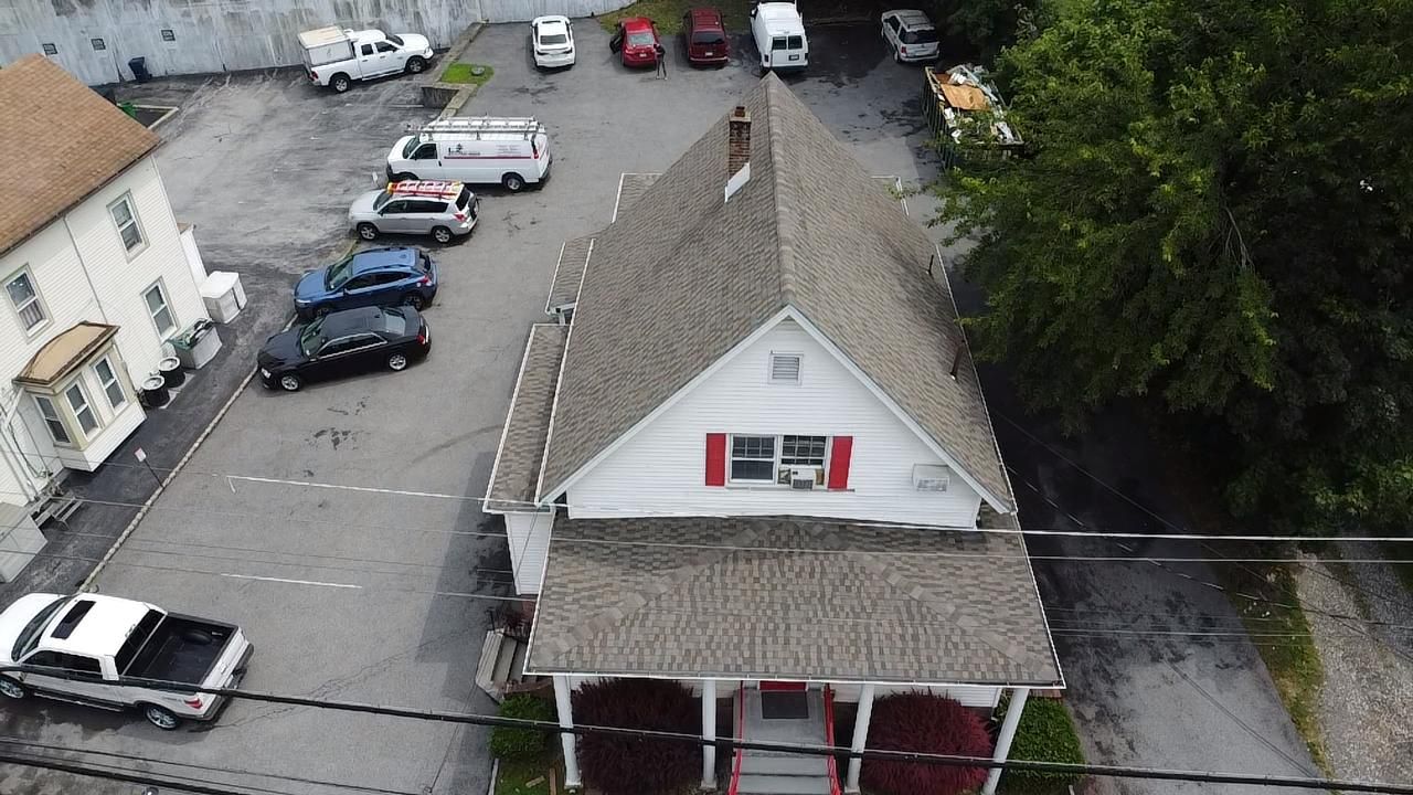 A house with a red door and window shutters, a parking lot with cars, and trees.