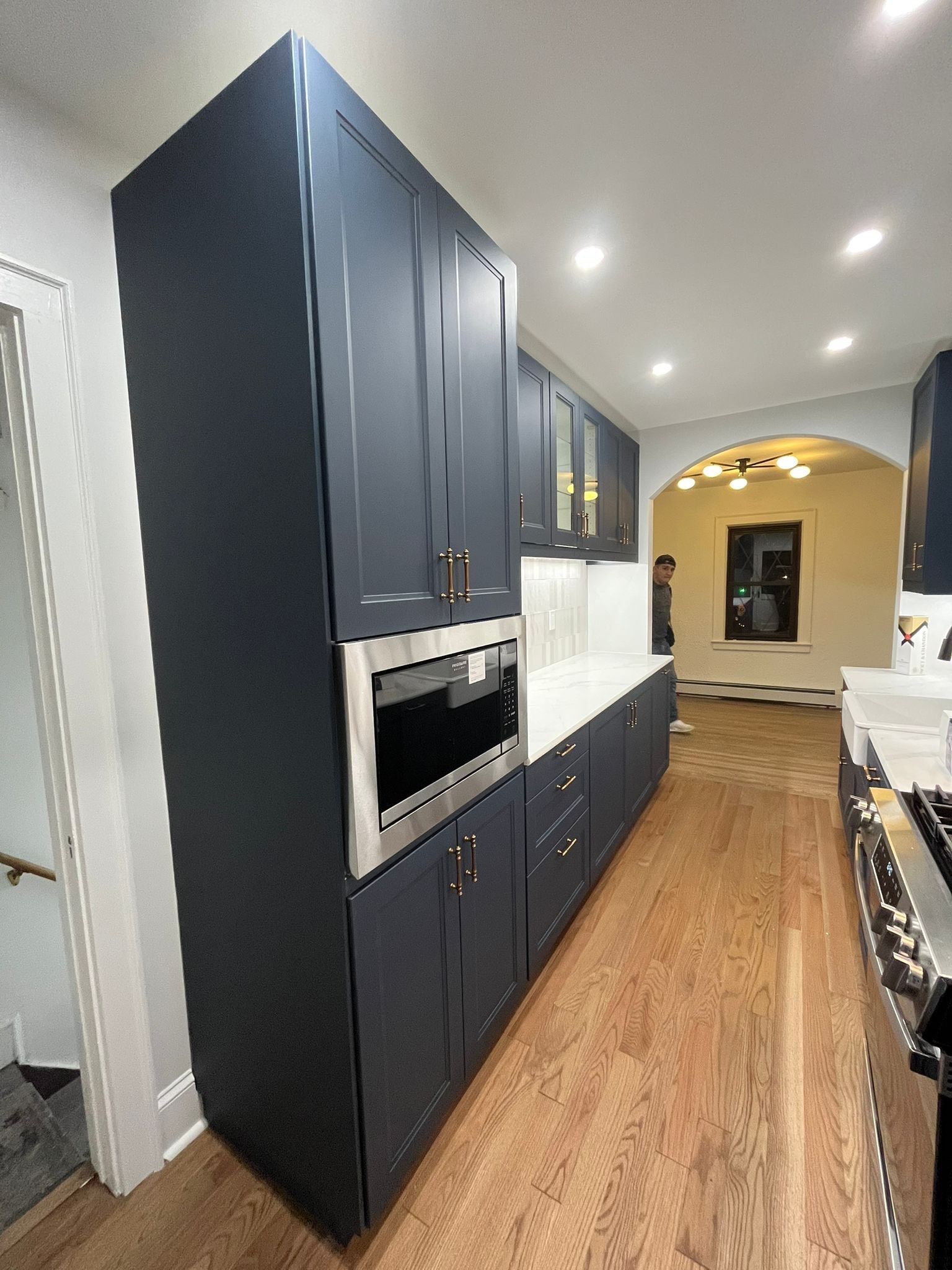 Dark blue kitchen cabinets with a built-in microwave, white countertop, and wooden floor.