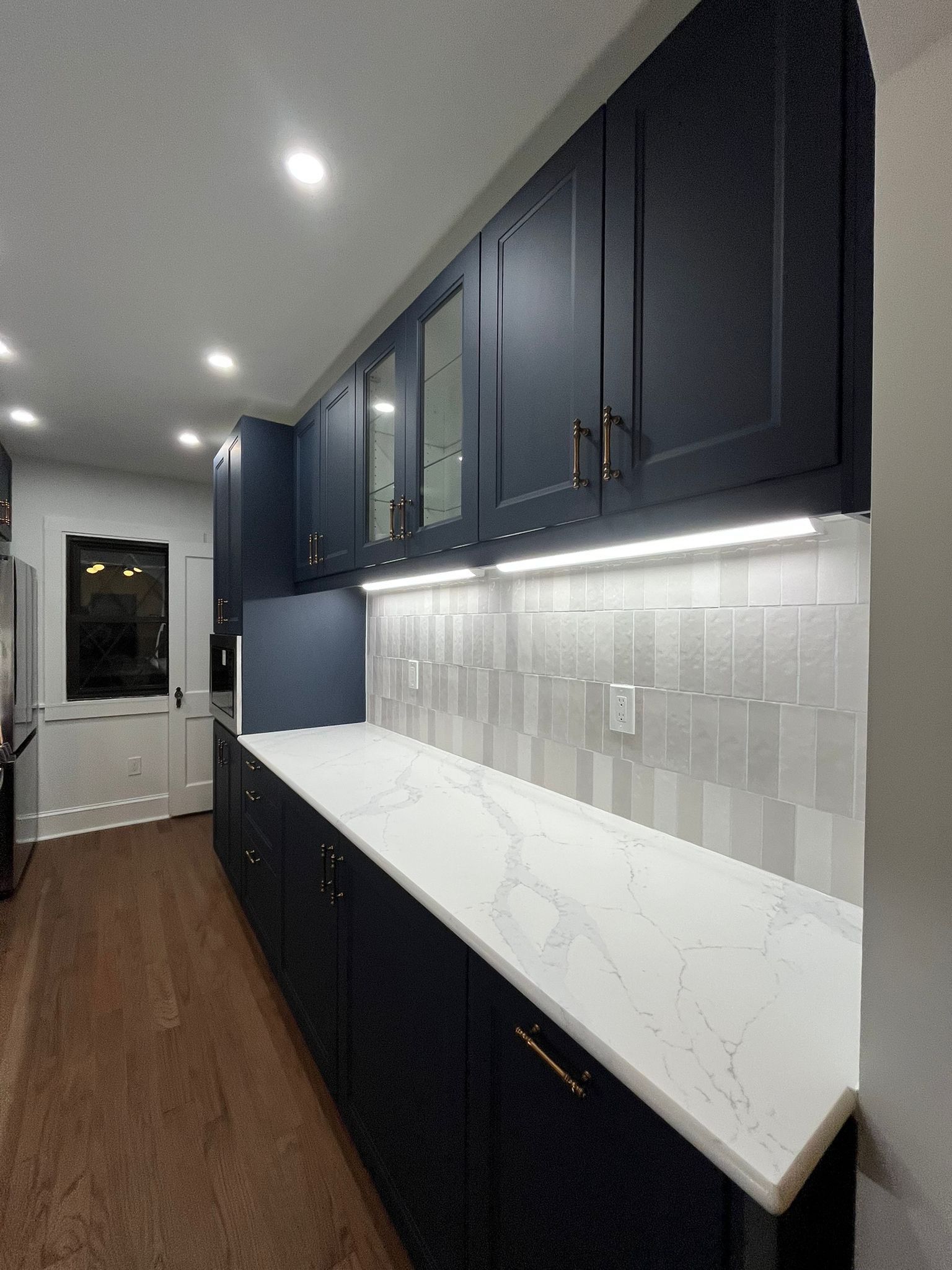 Navy blue kitchen with white countertops and backsplash, dark wood floor, and overhead lighting.