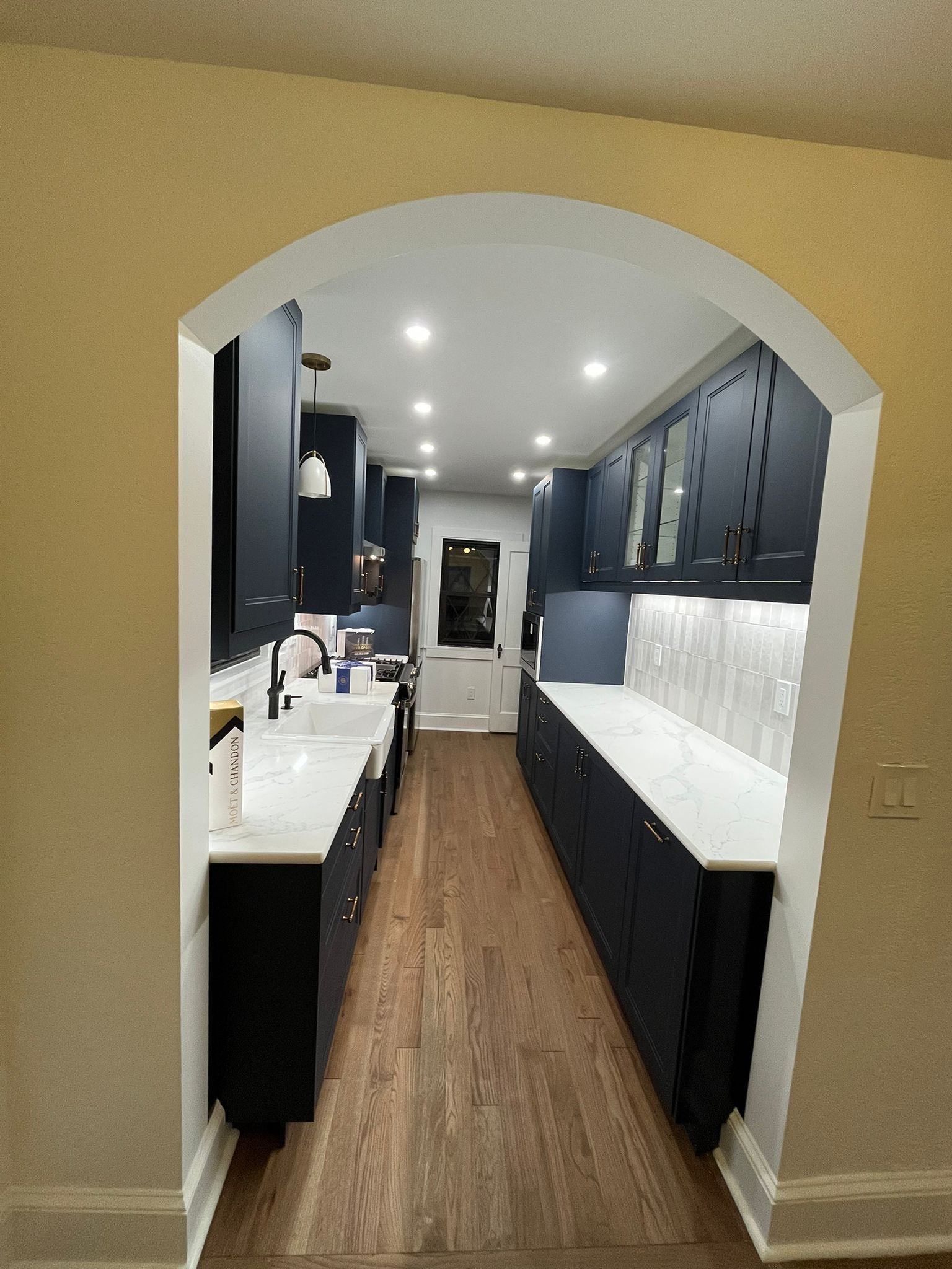 Dark blue kitchen with white countertops, an archway, and wooden floors.