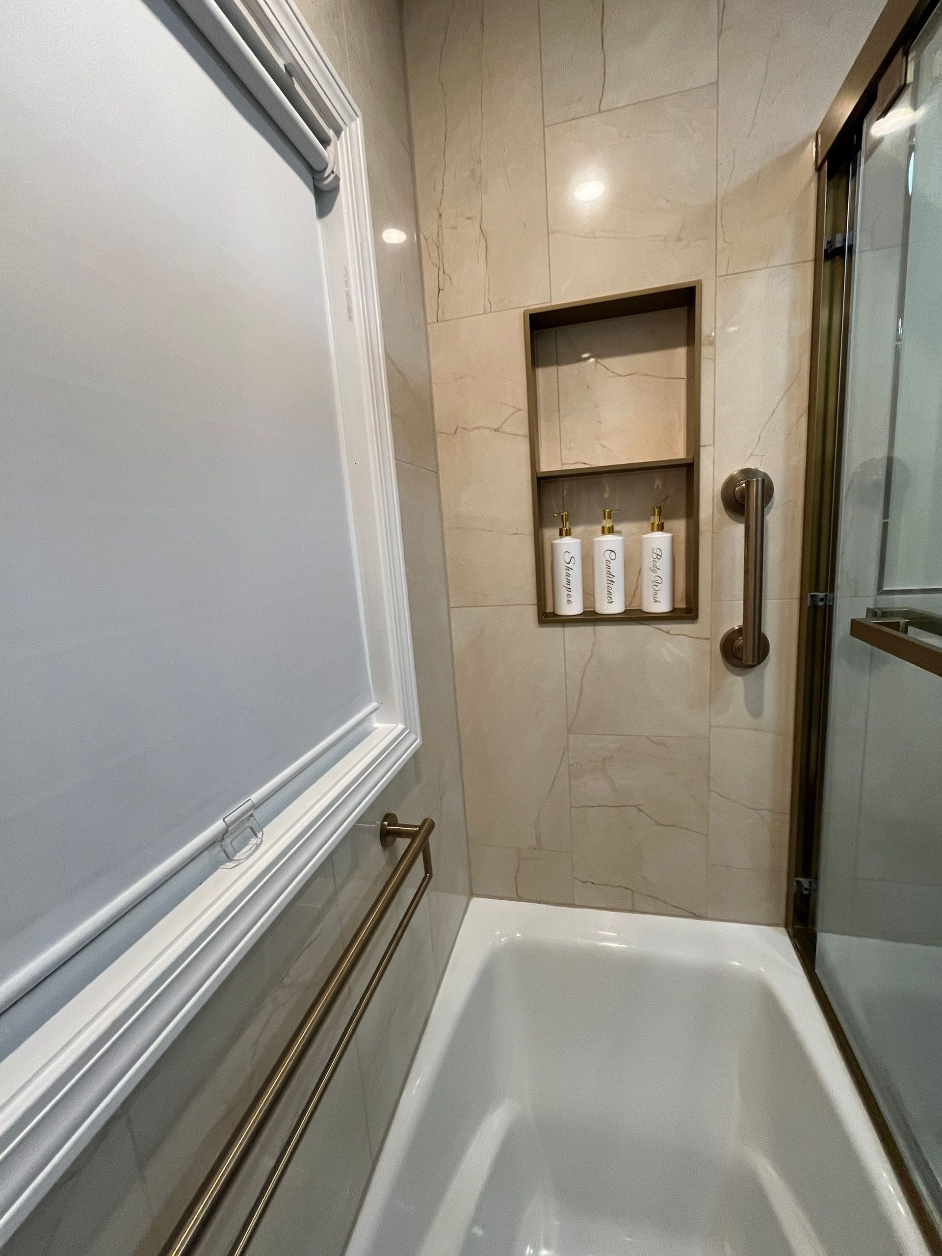 Bathroom with a tub, tiled walls, built-in shelf for toiletries, and a grab bar.