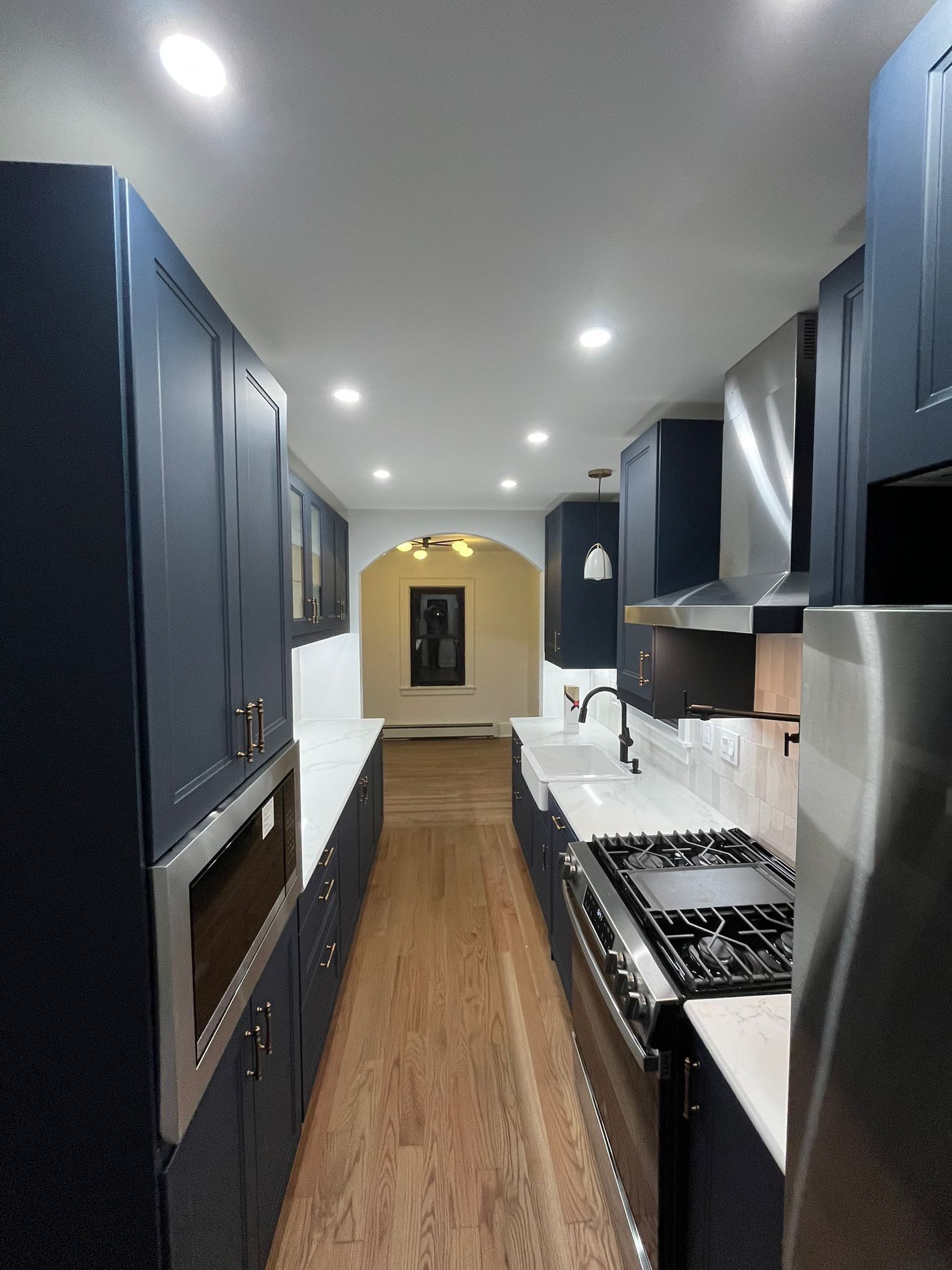 Narrow galley kitchen with navy cabinets, stainless steel appliances, and wood floors.