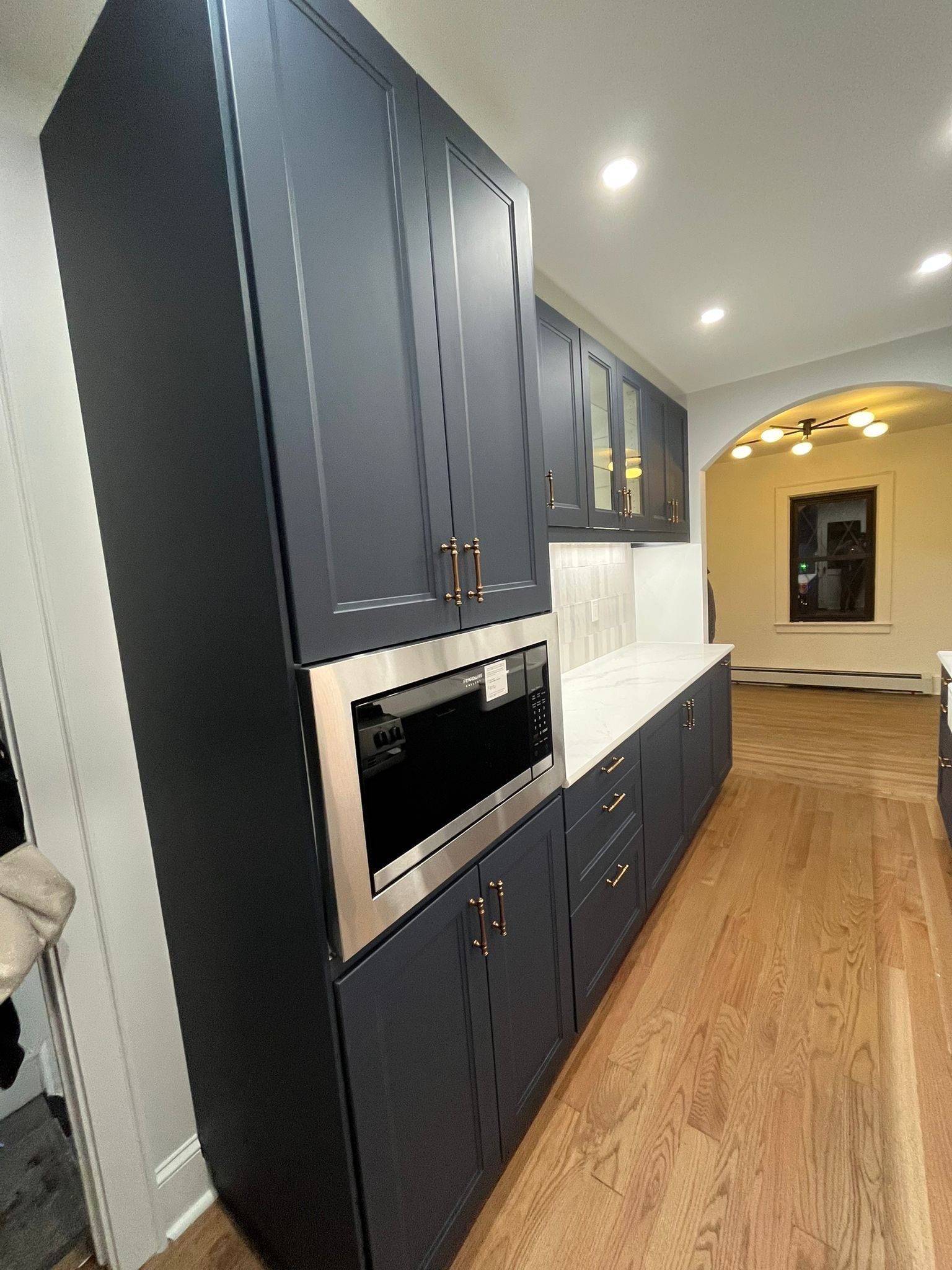 Dark blue kitchen cabinets with stainless steel microwave, white countertop, and wood floor.