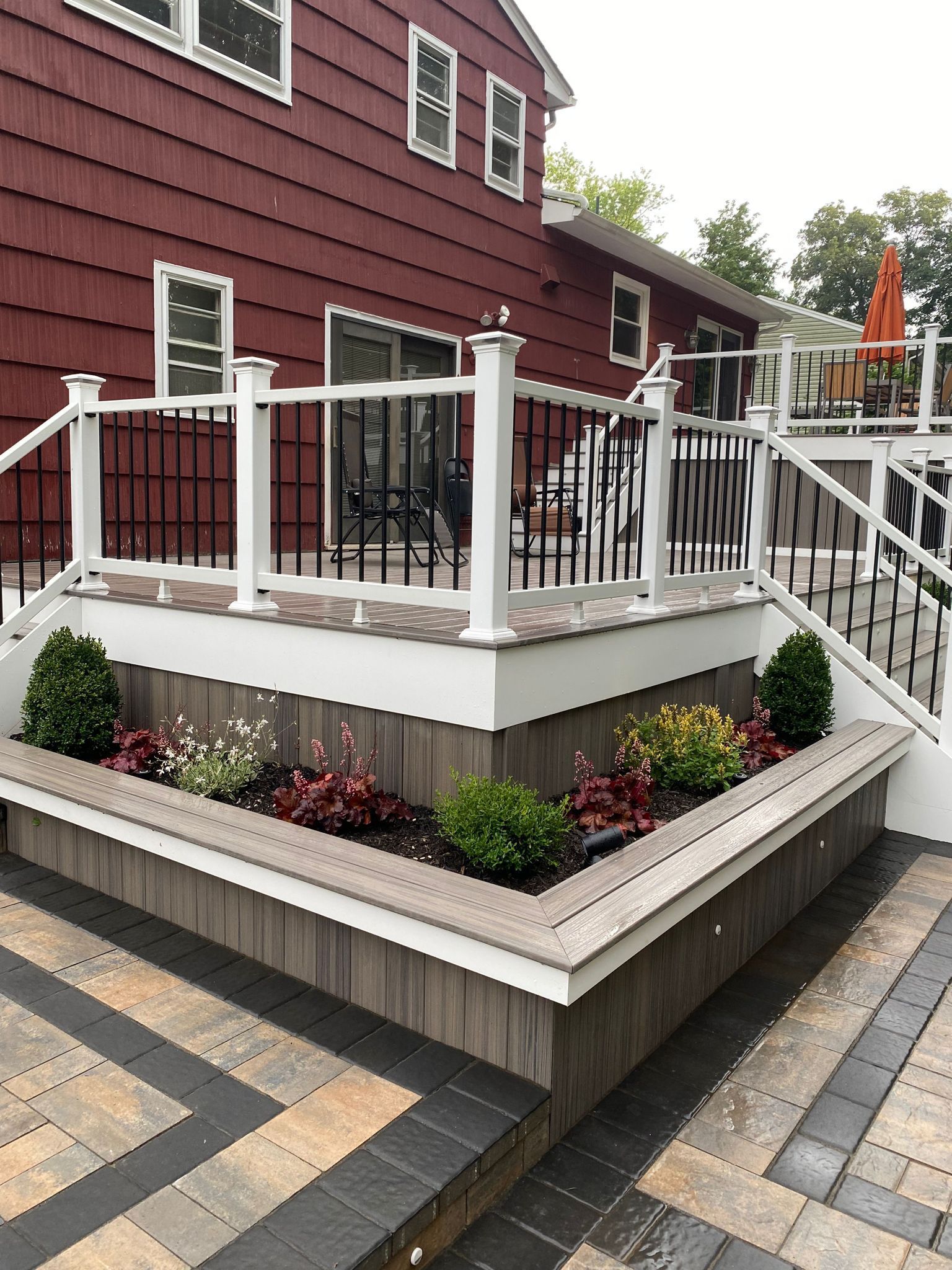 Raised deck with planter boxes, dark siding, and patterned paving.