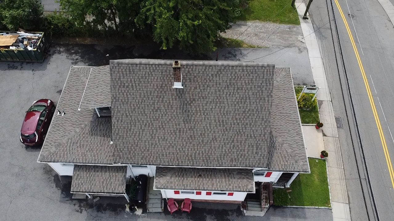 Overhead view of a gray-roofed building with a red car parked nearby and a road on the right.