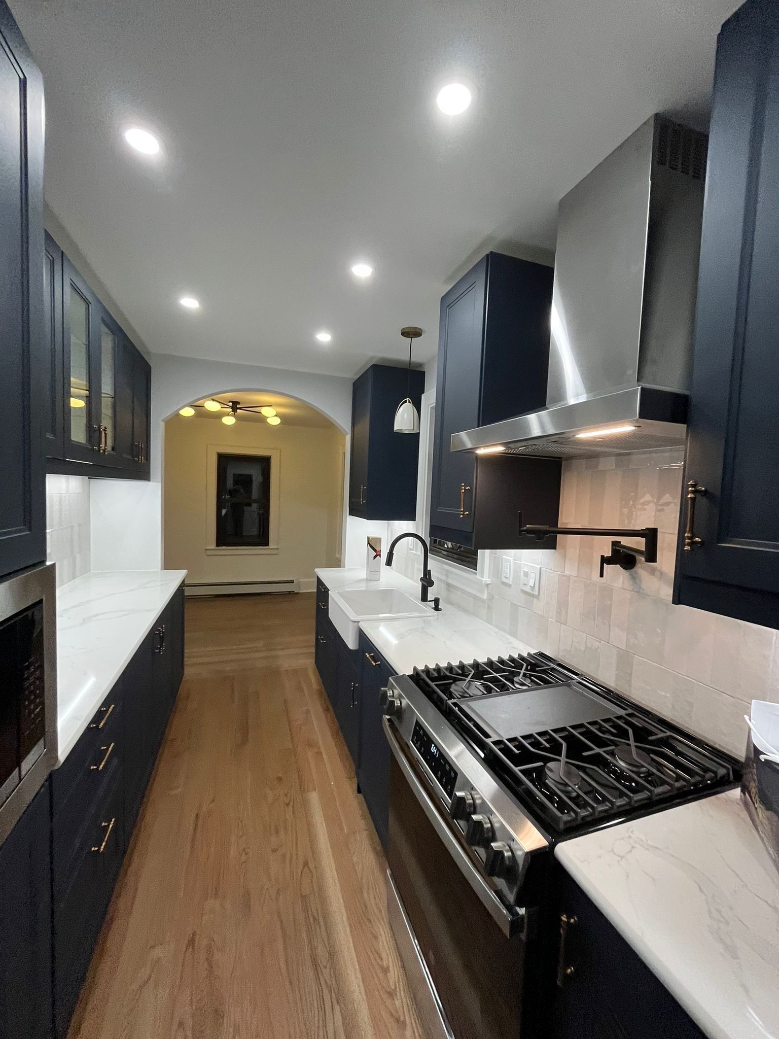 Navy blue kitchen with stainless steel appliances, white countertops, and light wood floors.