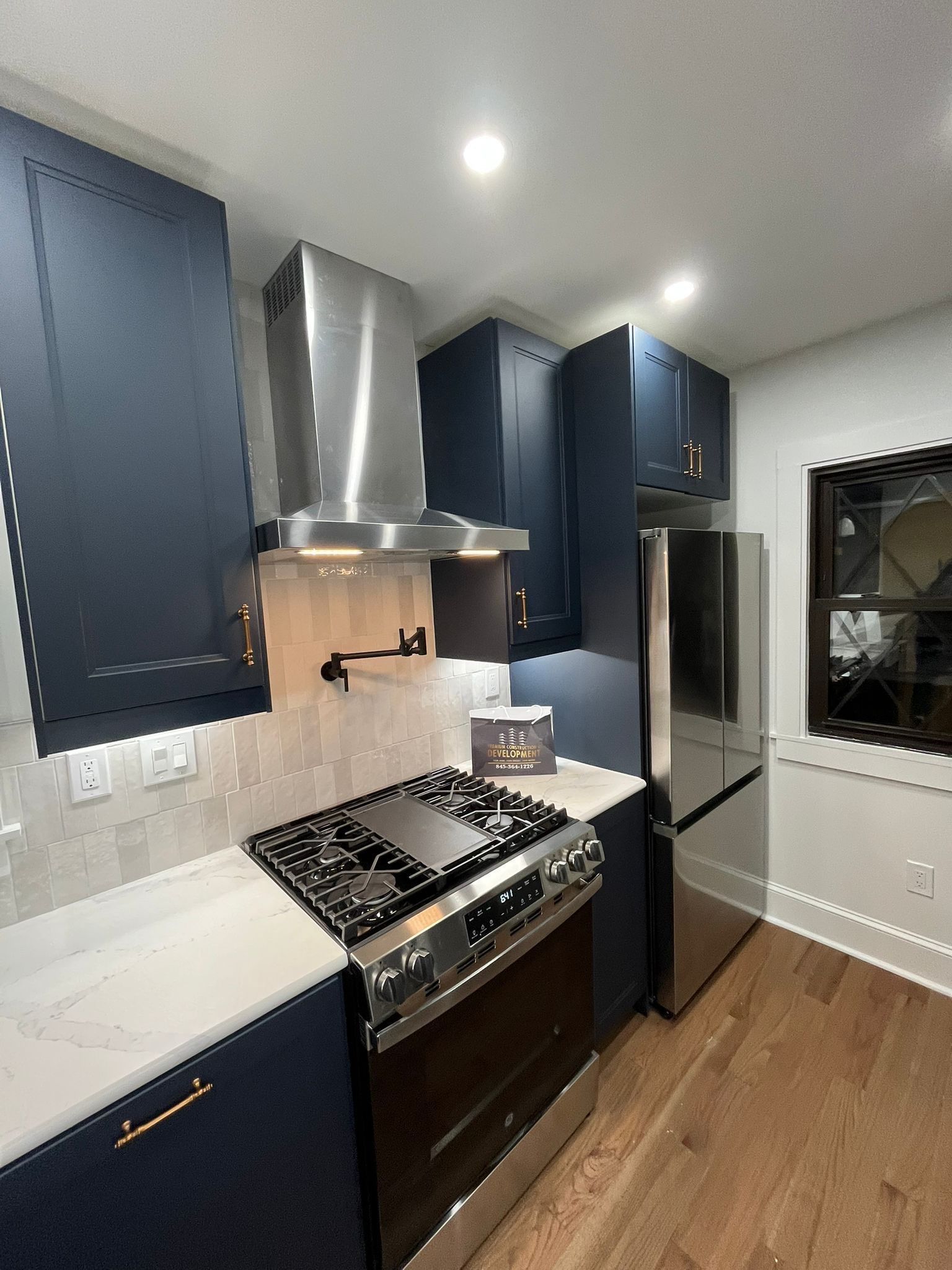 Modern kitchen with navy blue cabinets, stainless steel appliances, and a white countertop.