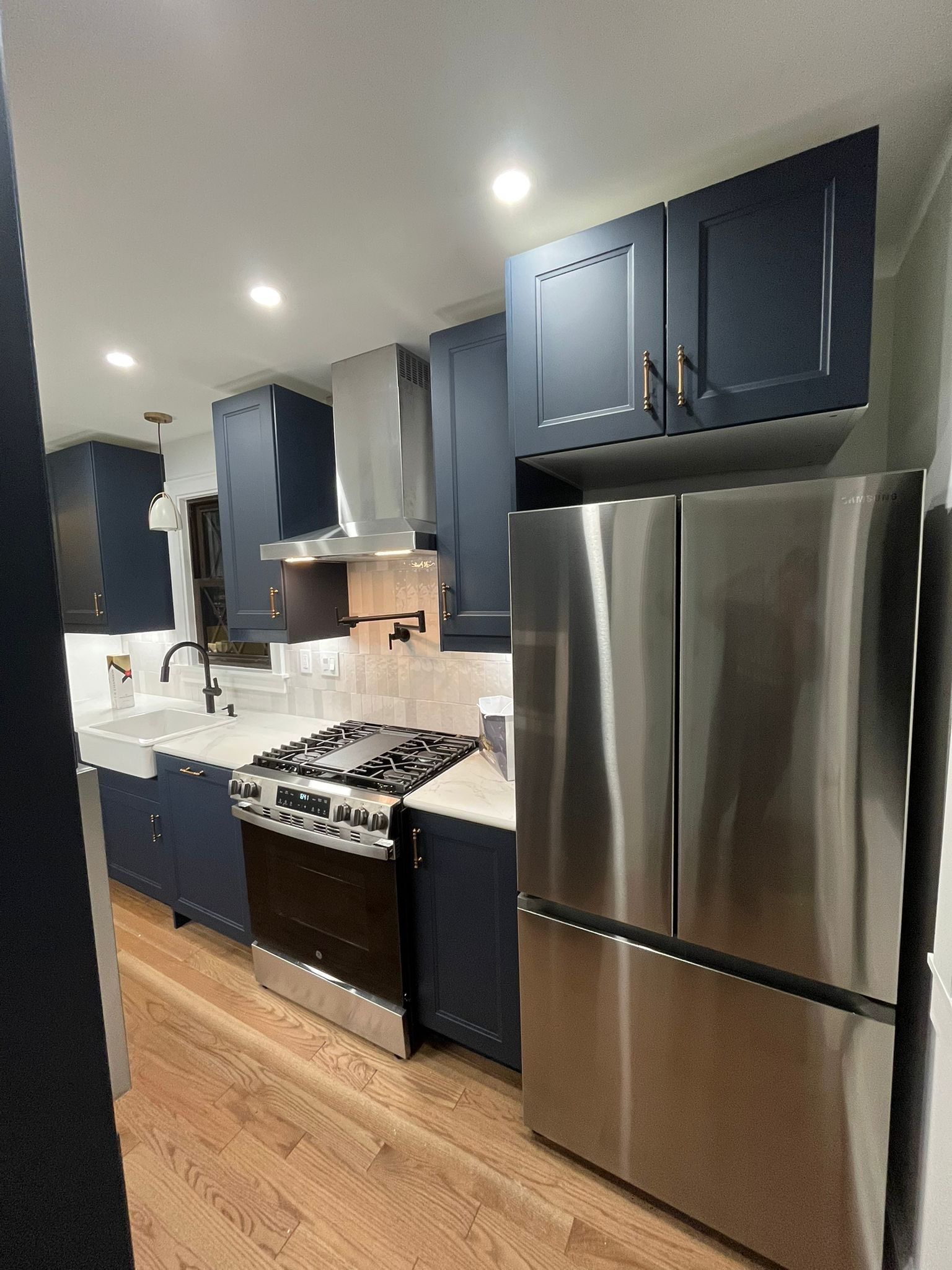 Navy blue kitchen with stainless steel appliances and light wood floors.