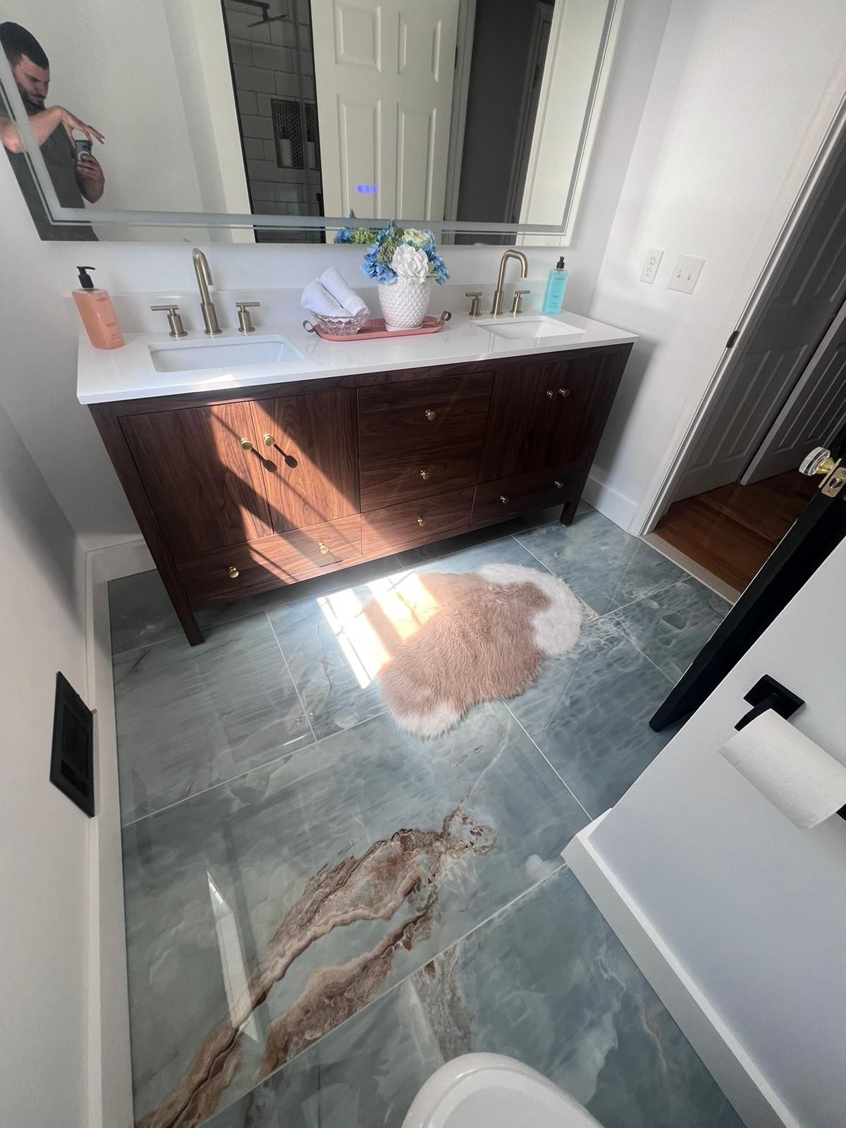 Bathroom with a dark wooden vanity, marble countertop, patterned blue-gray floor, and a light brown rug.