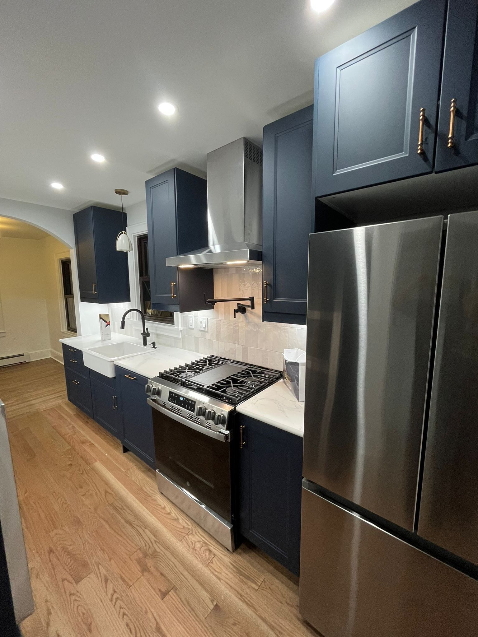 Navy blue kitchen with stainless steel appliances and light wood floors.