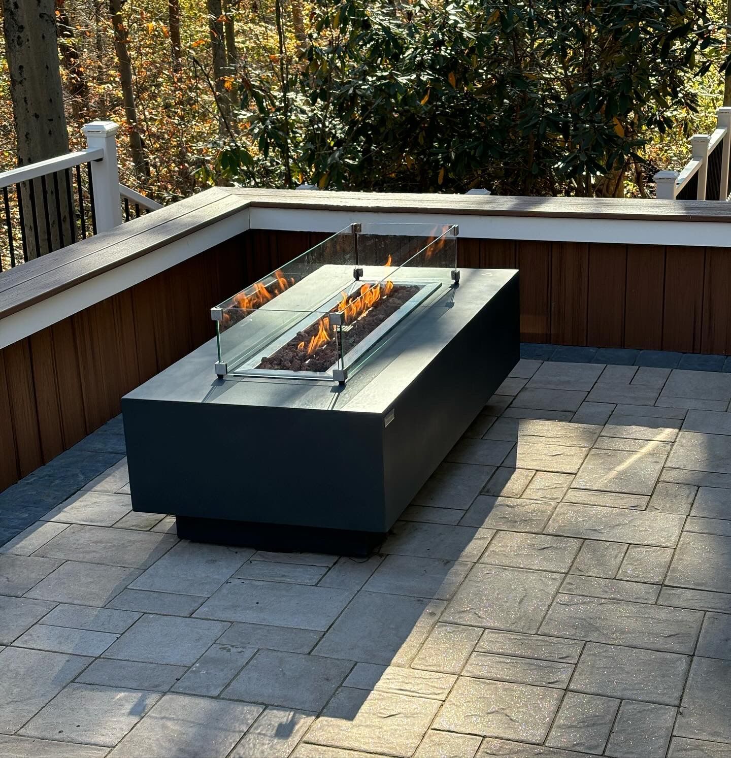Modern rectangular fire pit on a stone patio, with glass wind guards.