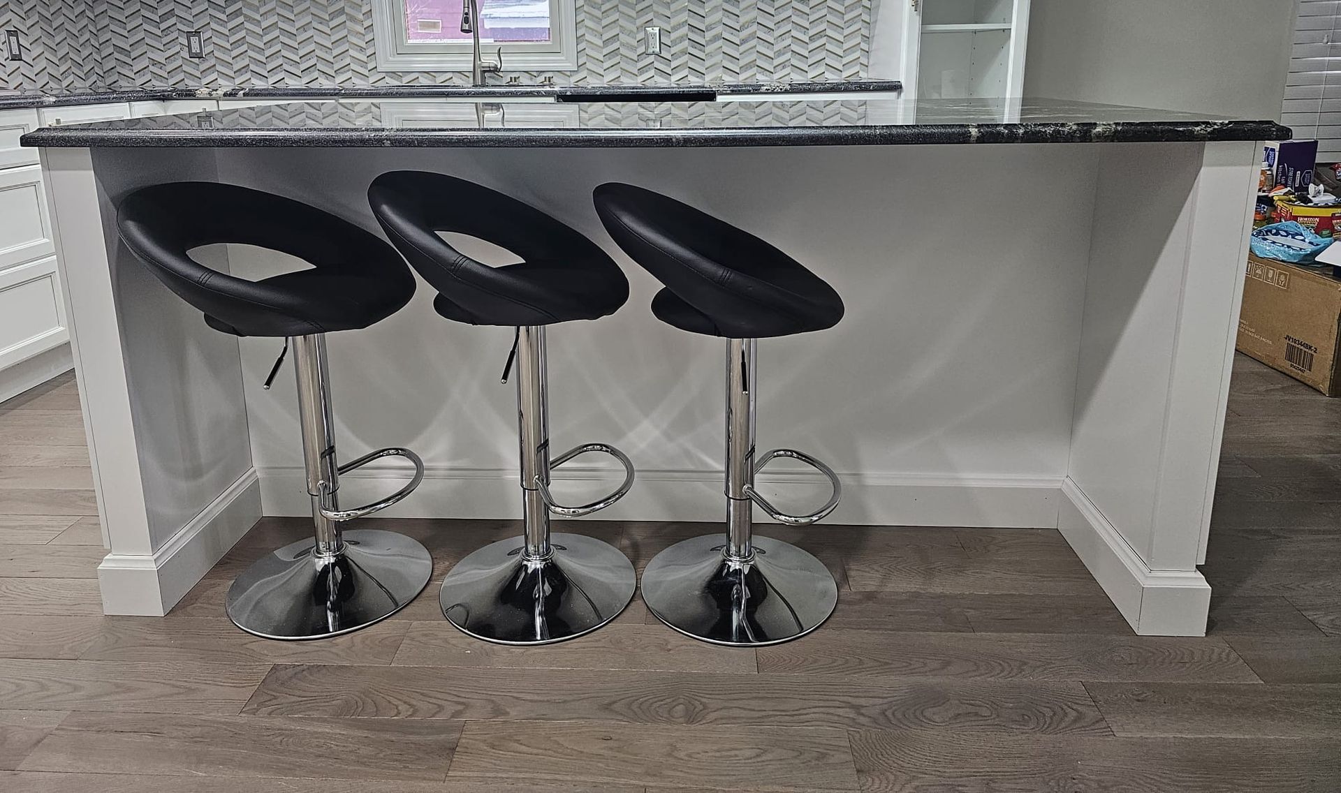 Three black bar stools at a white kitchen island with a black countertop, in a kitchen.