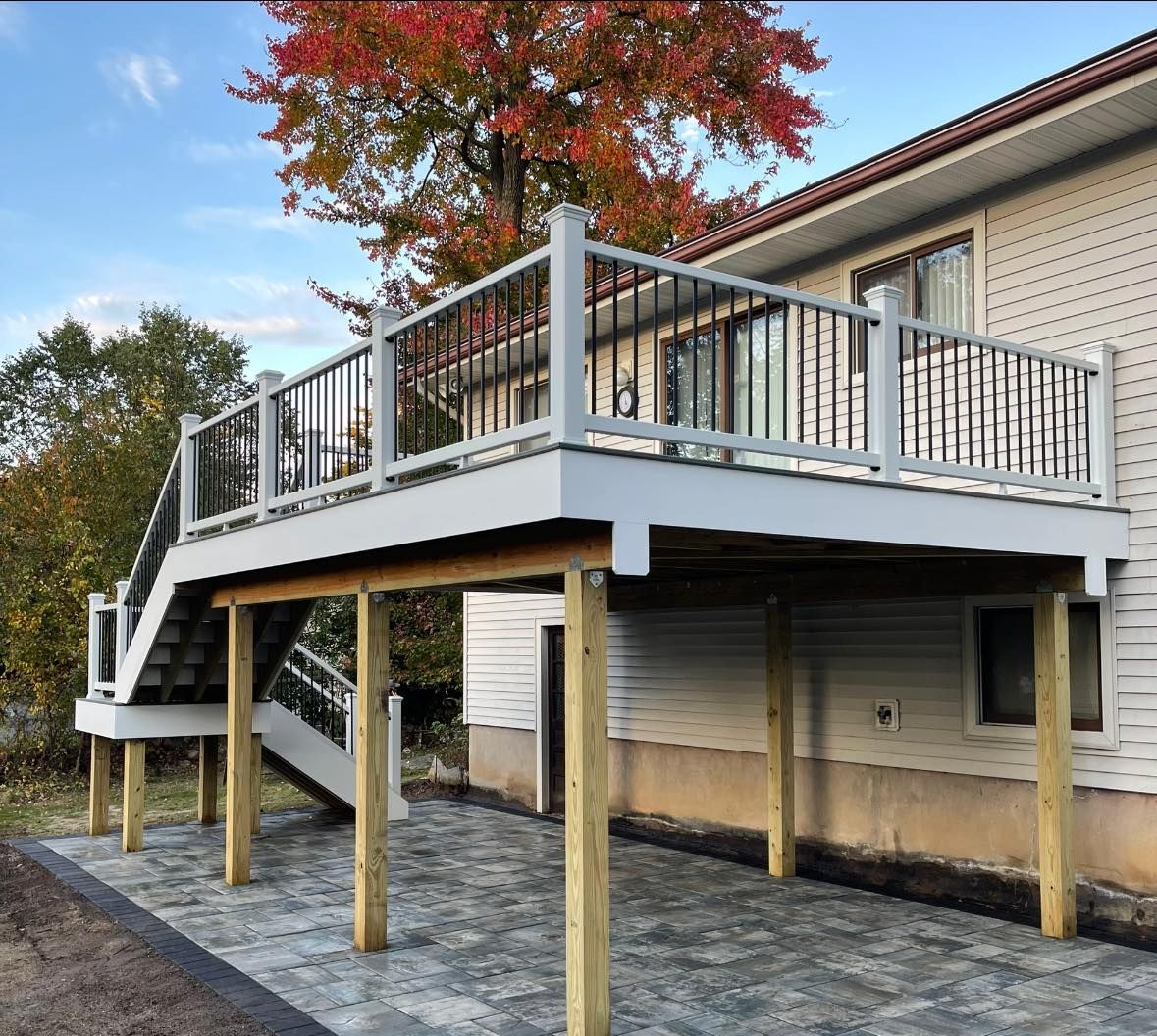 Elevated deck with stairs, supported by wooden posts, with a house in the background. Gray and white structure.