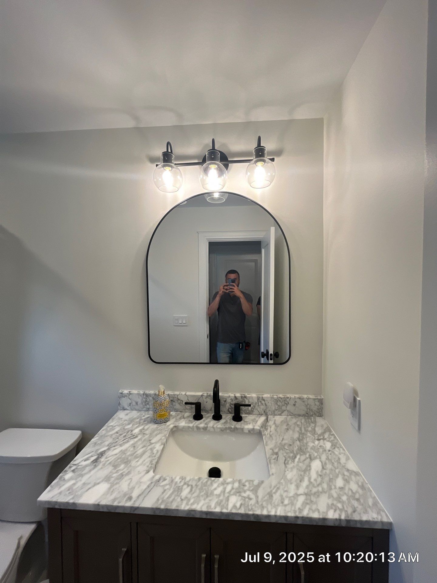 Bathroom with vanity, mirror, and lights; person taking photo reflected in mirror.