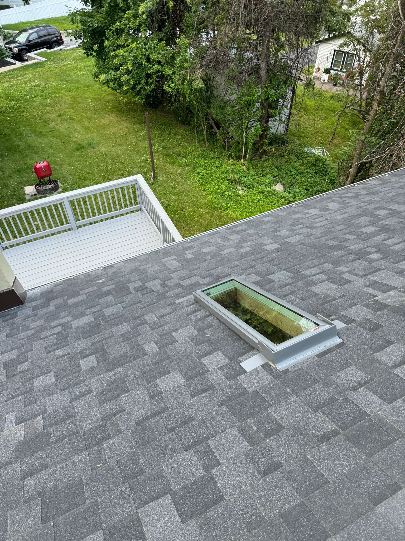 Gray shingled roof with a skylight and view of a yard with a deck.