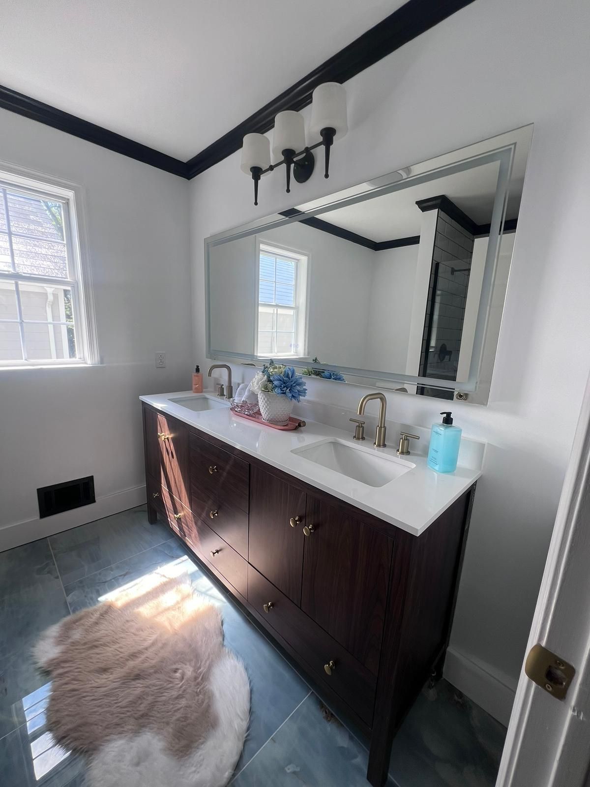 Bathroom with dark wood vanity, white countertop, large mirror, window, and fur rug.