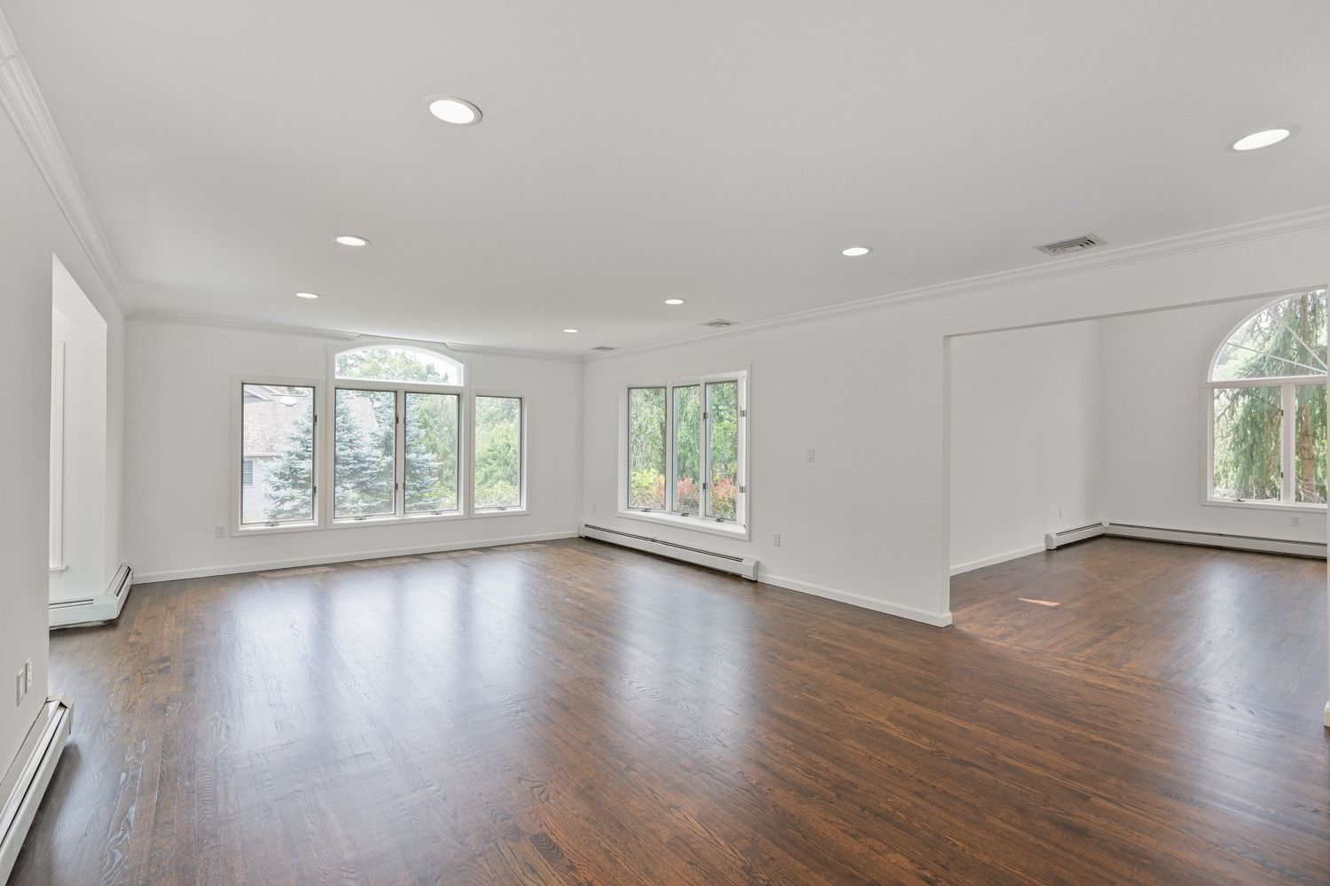 Empty, bright living room with dark wood floors, white walls, and large windows.