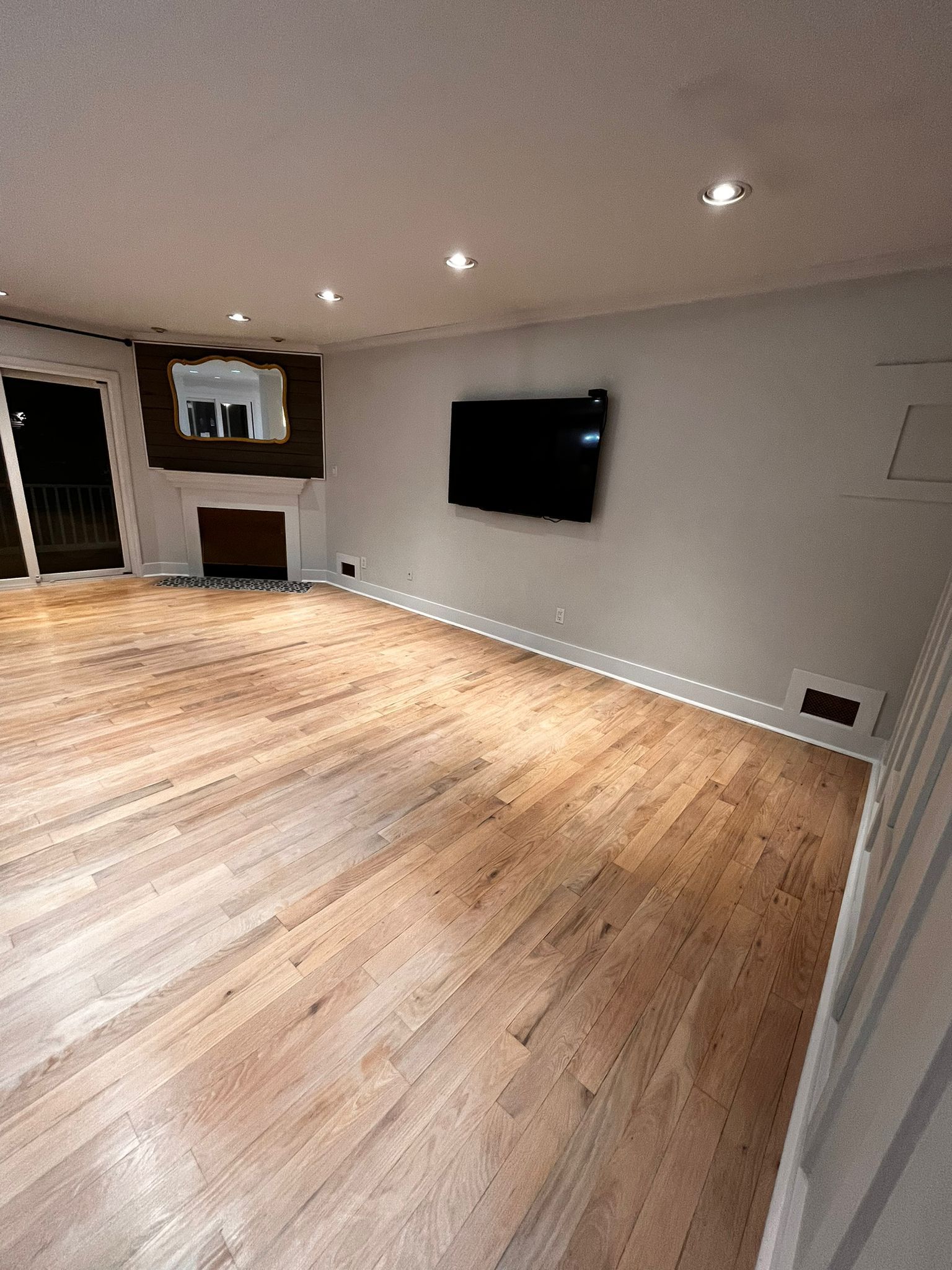 Empty room with light wood floors, white walls, fireplace, and a mounted TV.