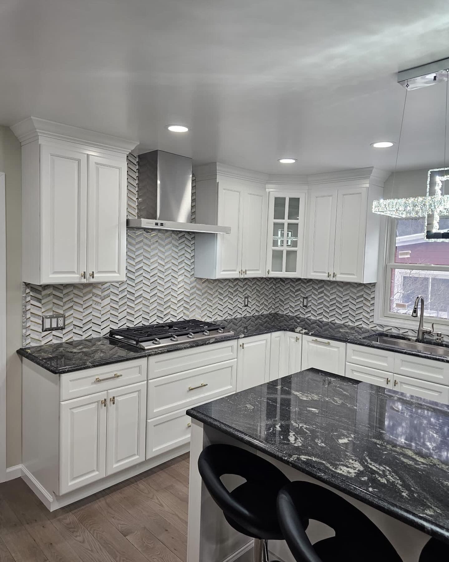 White kitchen with dark countertops, stainless steel range hood, and black bar stools.