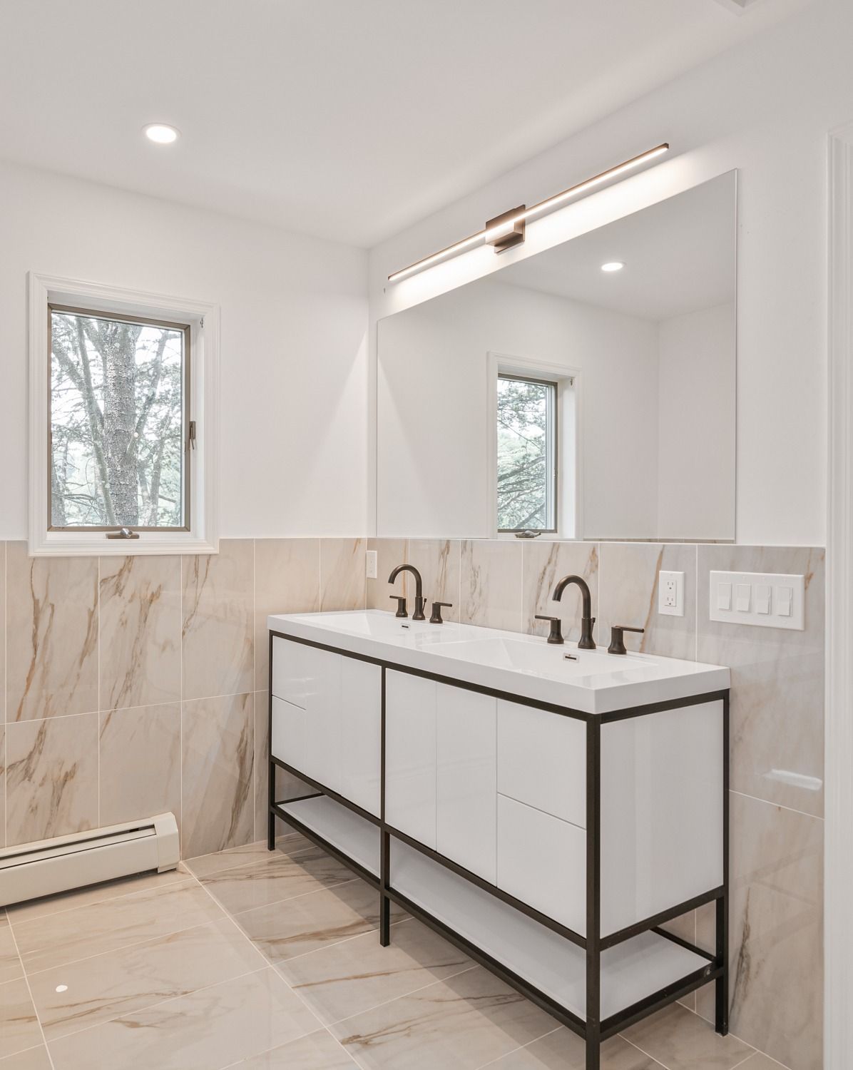 Modern white bathroom with marble tile, double vanity, large mirror, and black fixtures.