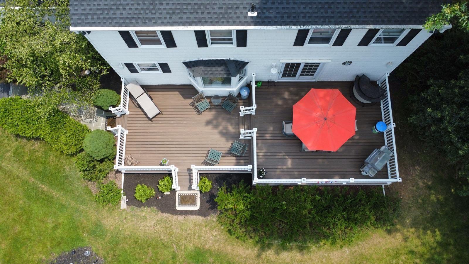 Aerial view of a two-story house with a large wooden deck, red umbrella, and yard.