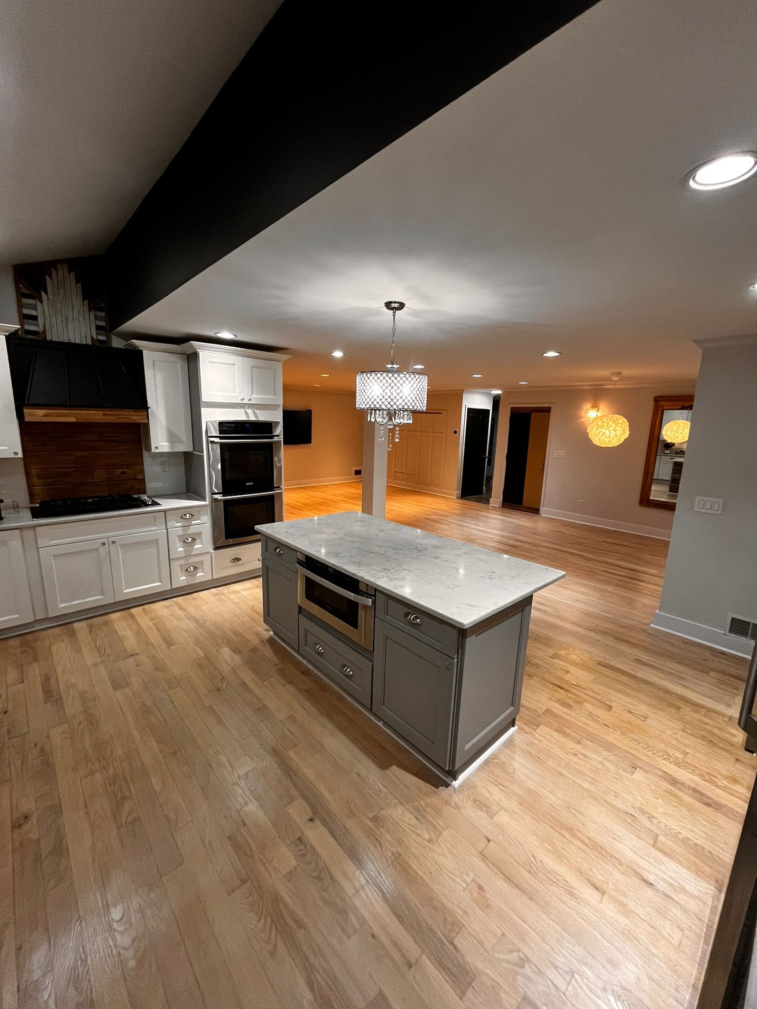Open-concept kitchen with wooden floors, grey cabinets, island, and a black ceiling beam.