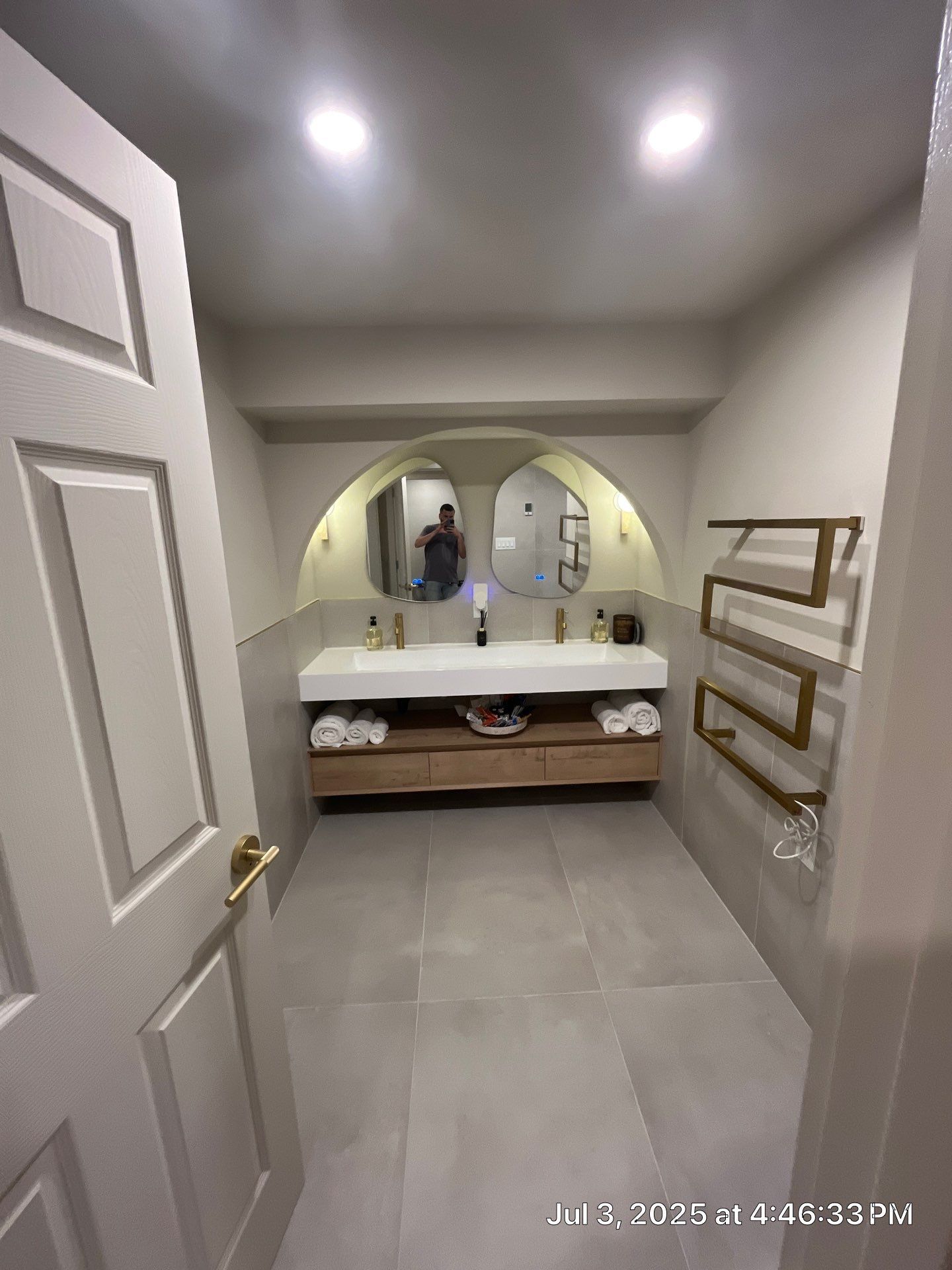 Bathroom with double vanity, two arched mirrors, and gold towel warmer.