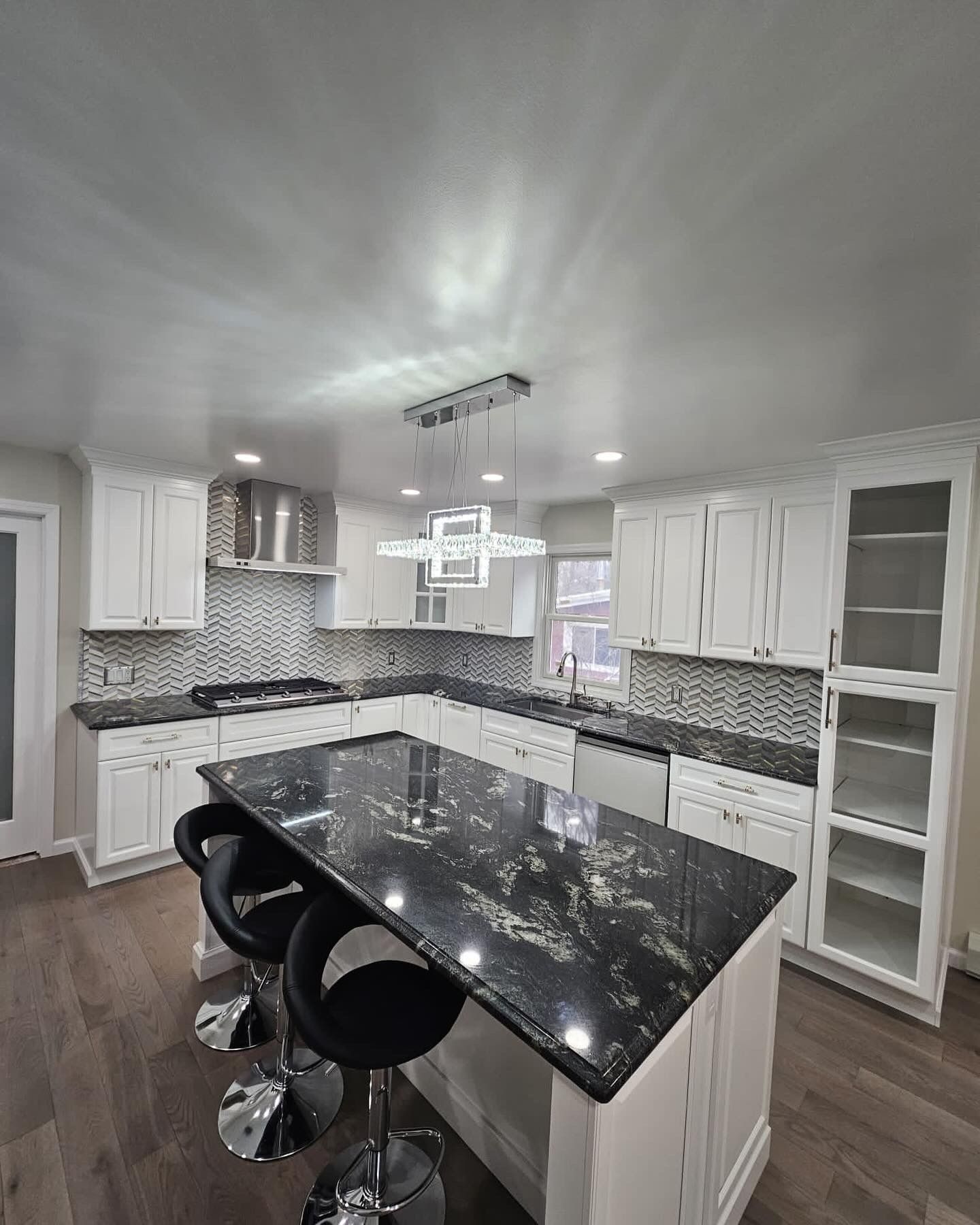 Modern white kitchen with a black granite island, stools, and white cabinets.