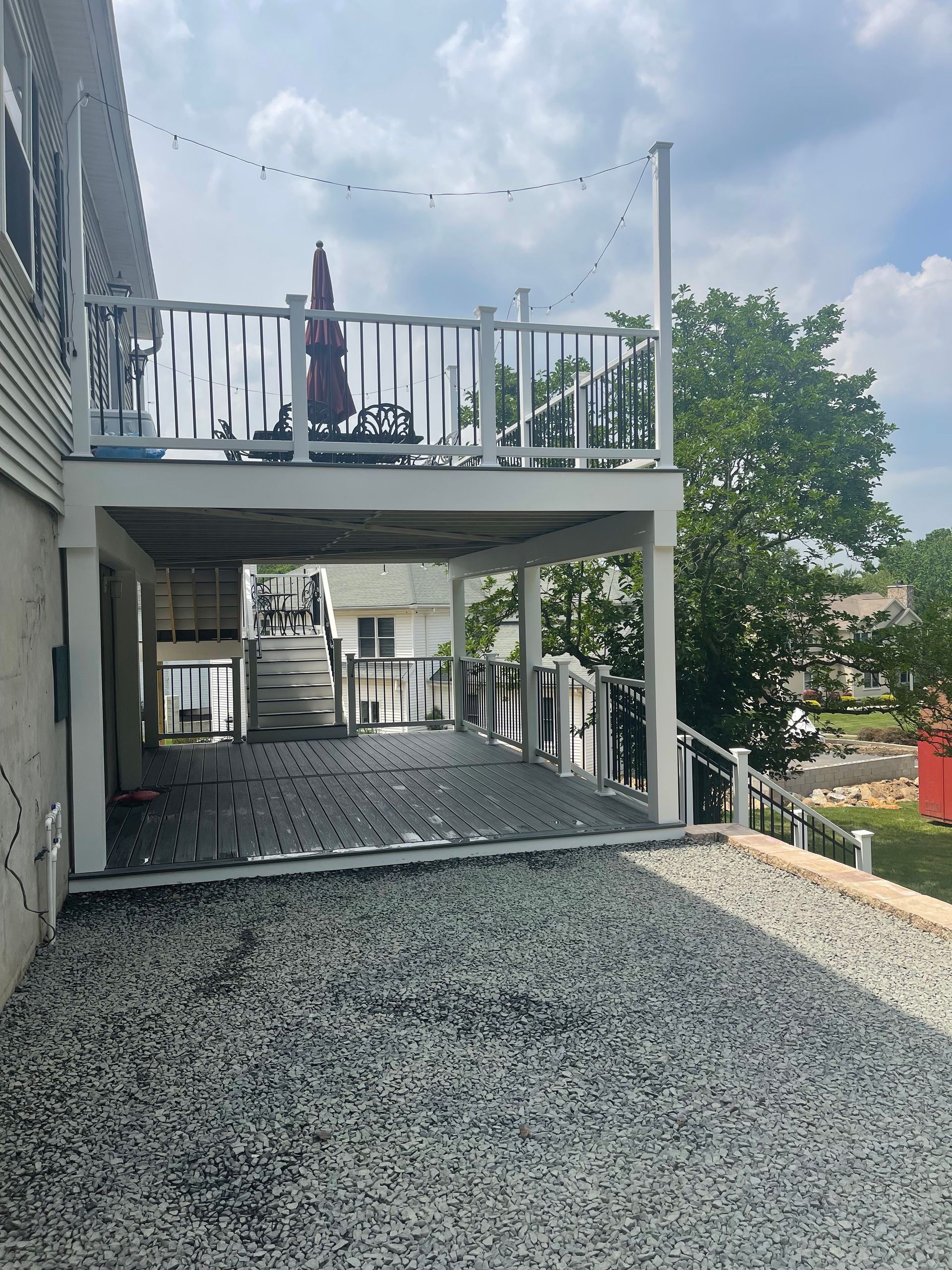 Two-level deck with gravel ground. Top level has a table, umbrella, and railing.