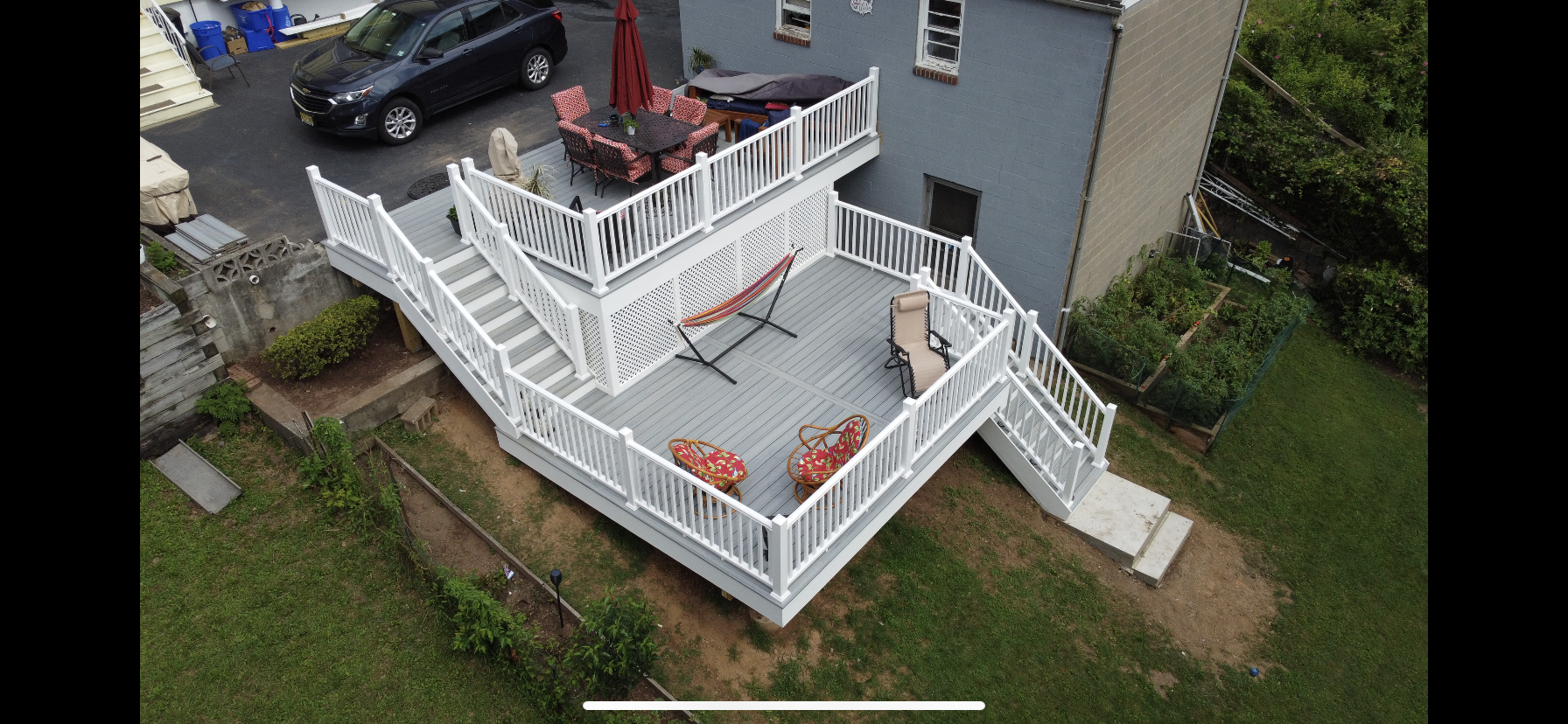 Overhead view of a multi-level deck with white railing and a gray house.  A car and lawn are also visible.
