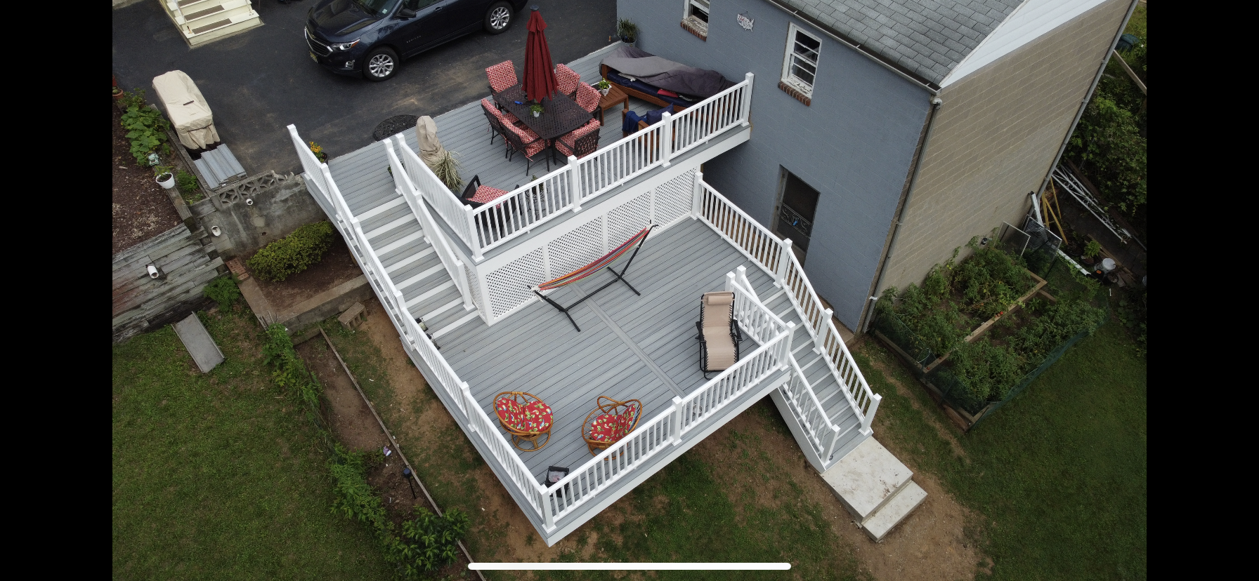 Aerial view of a multi-level white deck with furniture, attached to a gray house, with a car parked nearby.