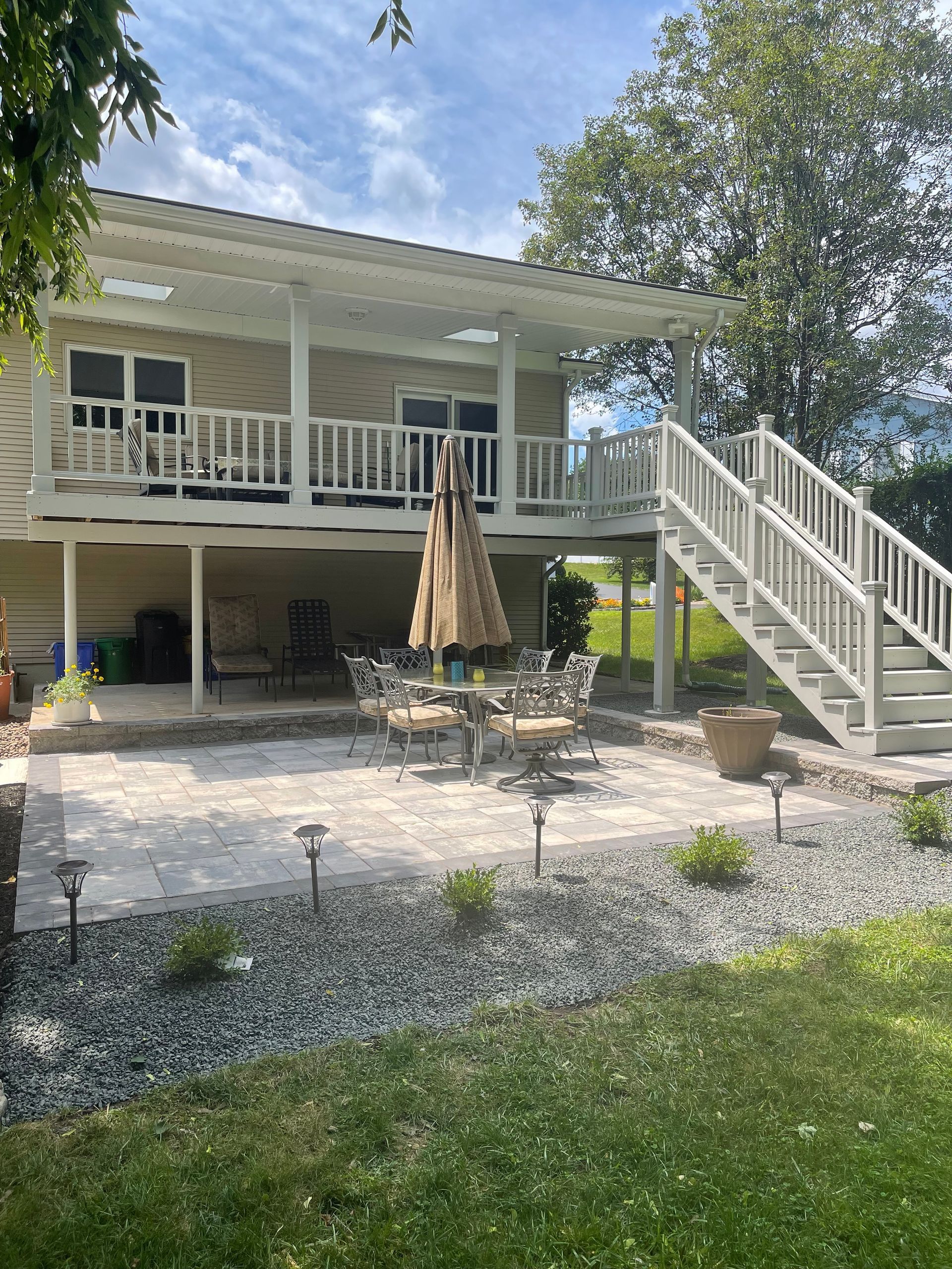 Beige house with a raised deck, stairs, and patio with a table and umbrella.