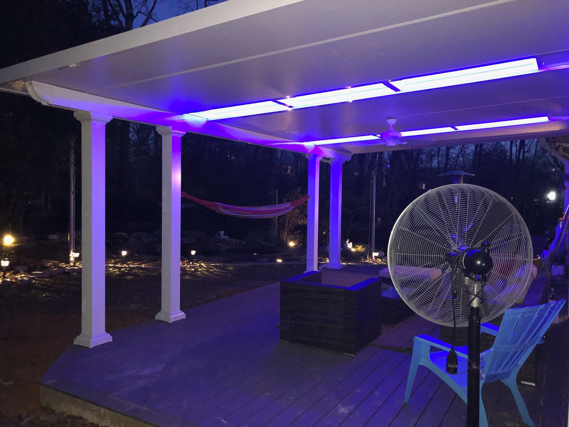 Patio with purple lighting under a white canopy, a fan, and a hammock at night.