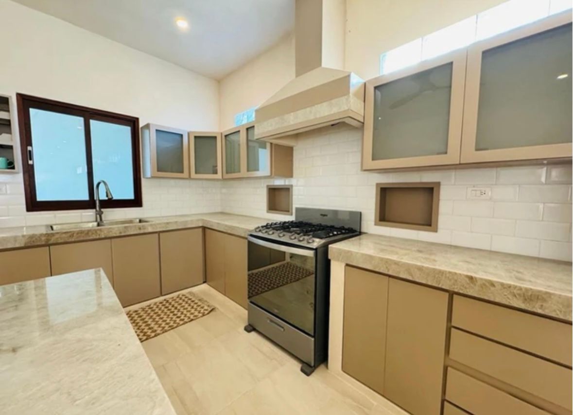 Modern kitchen with tan cabinets, gray countertops, stainless steel oven, and neutral backsplash.