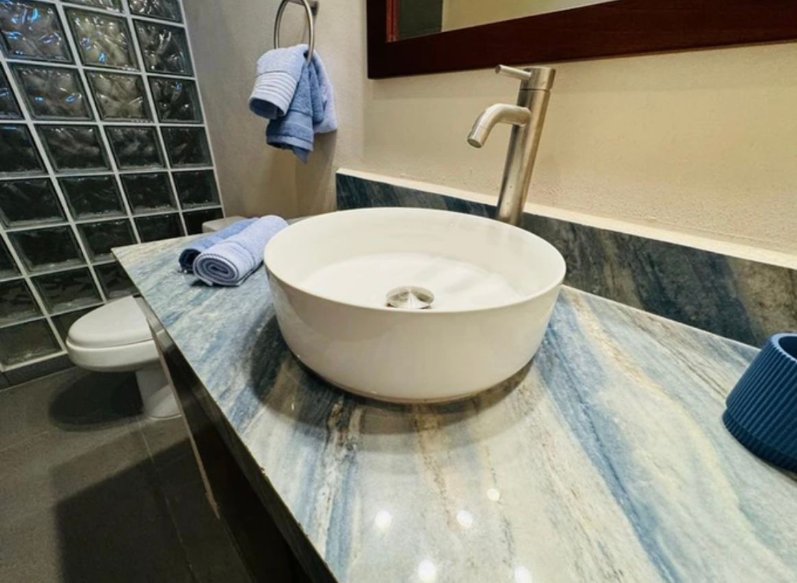 Bathroom with white vessel sink on blue marble countertop, blue towels, and glass block wall.