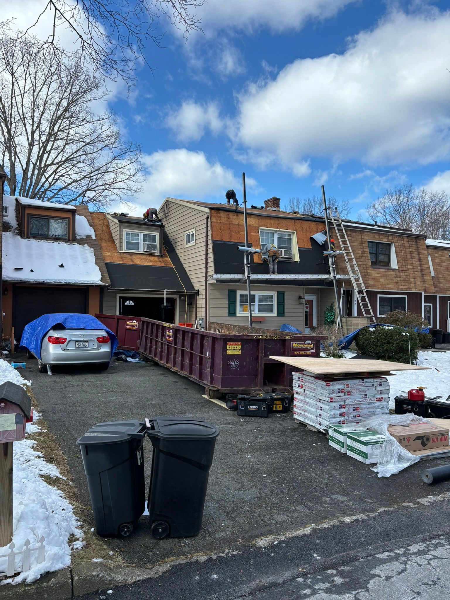 Roofing work on rowhouses; a dumpster, ladder, and materials are in front.